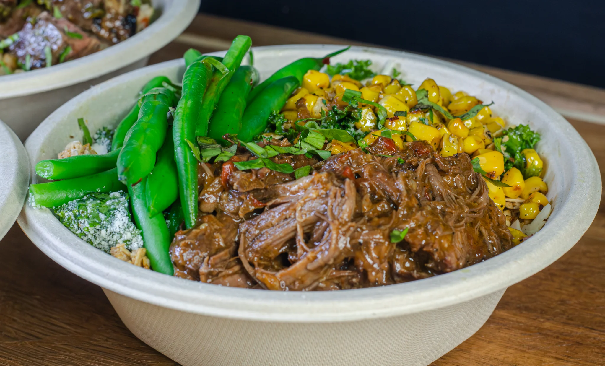 A bowl filled with tender beef, green beans, corn, and a mix of vegetables, garnished with herbs.