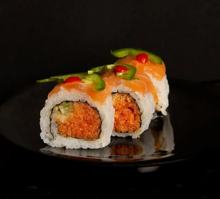 Delicious sushi roll topped with salmon and garnished with peppers.