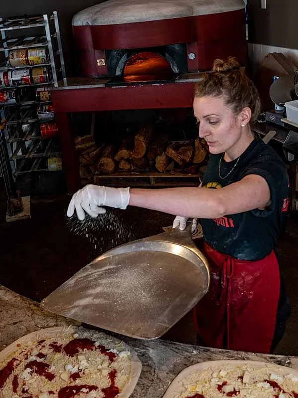 Chef preparing Margherita pizza in a wood-fired oven