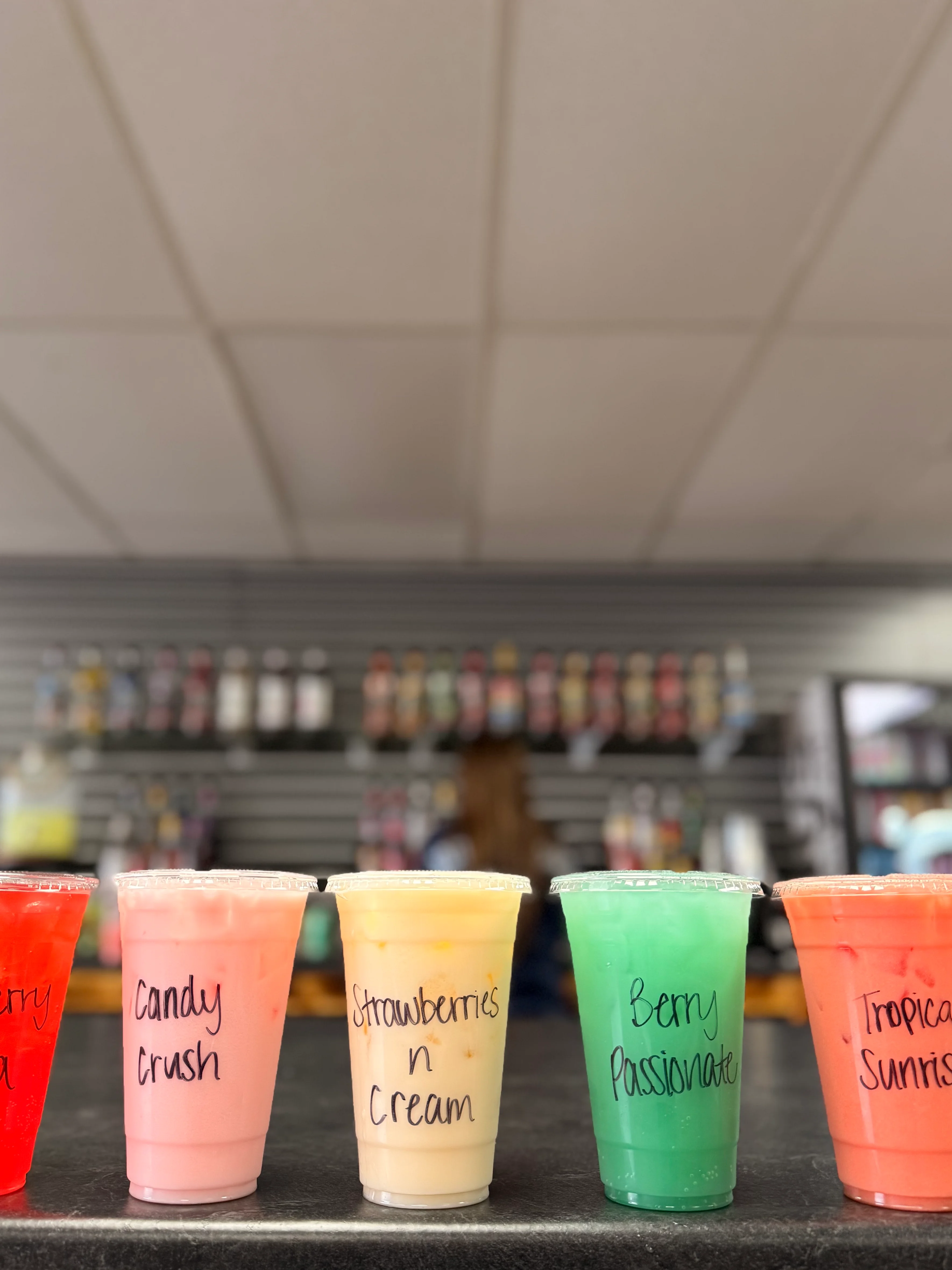 Five assorted drinks in clear cups, each labeled with different flavors, displayed on a countertop, showcasing vibrant colors.
