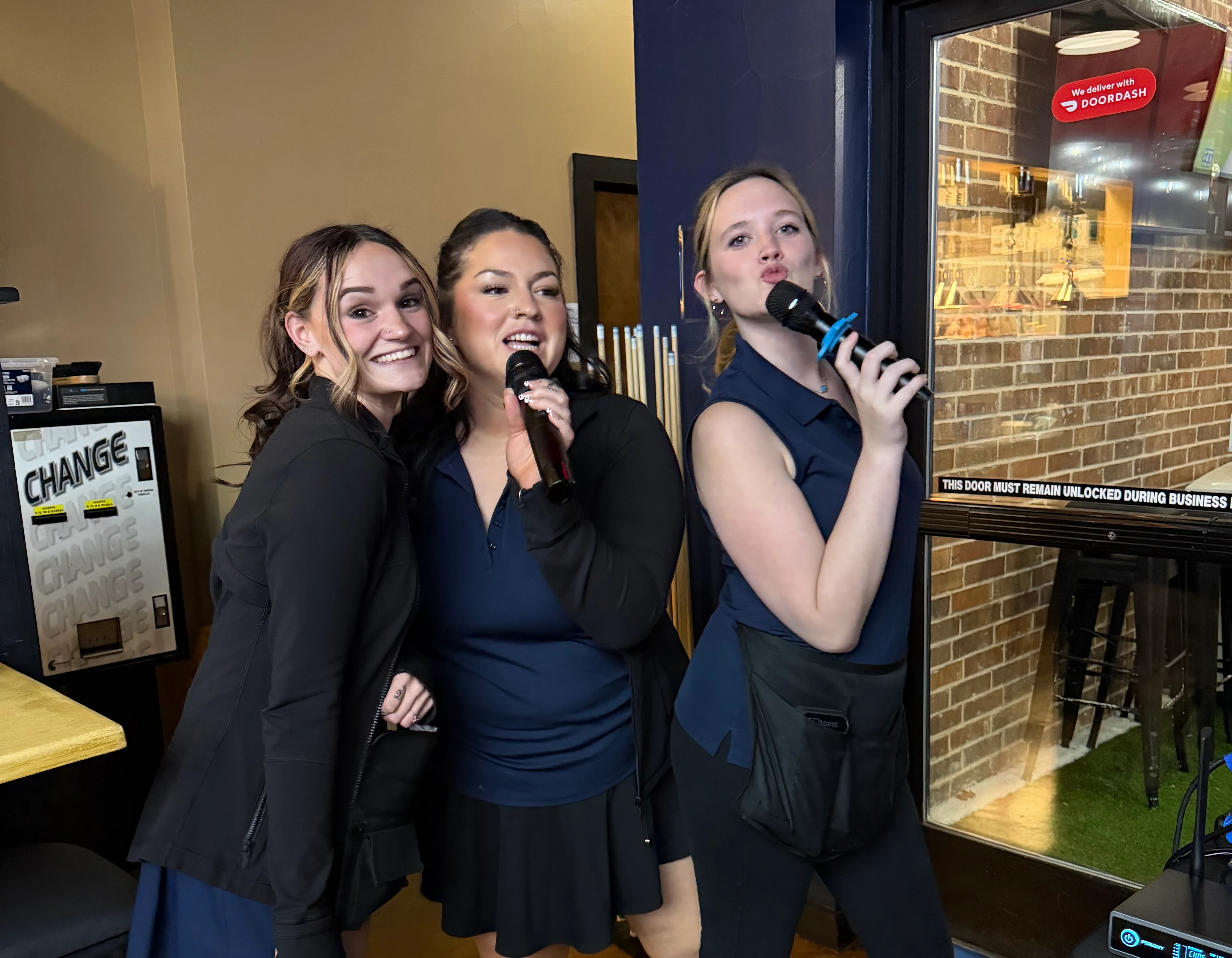 Three staff members singing with microphones in a lively restaurant setting