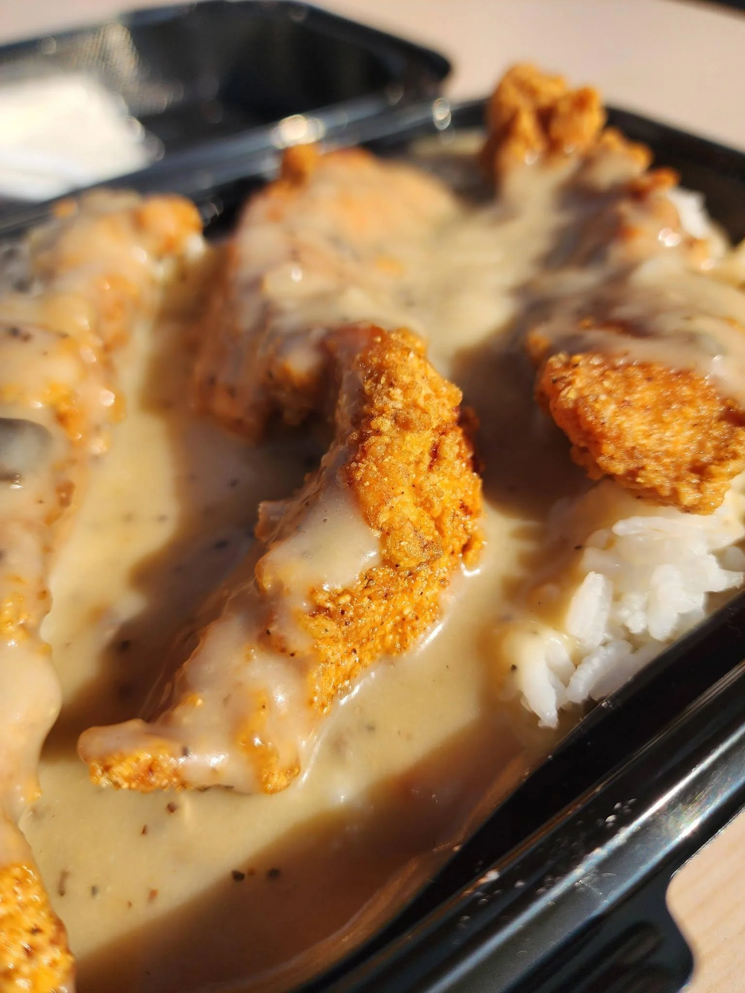 Crispy chicken tenders drizzled with gravy, served over rice.