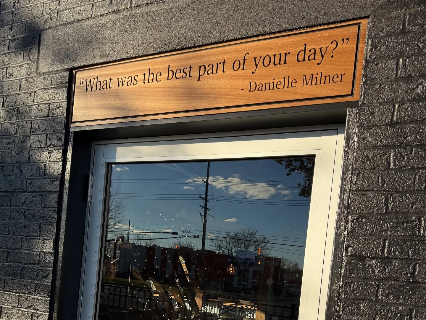A wooden sign above a storefront displaying the question, 'What was the best part of your day?' which is attributed to an individual.