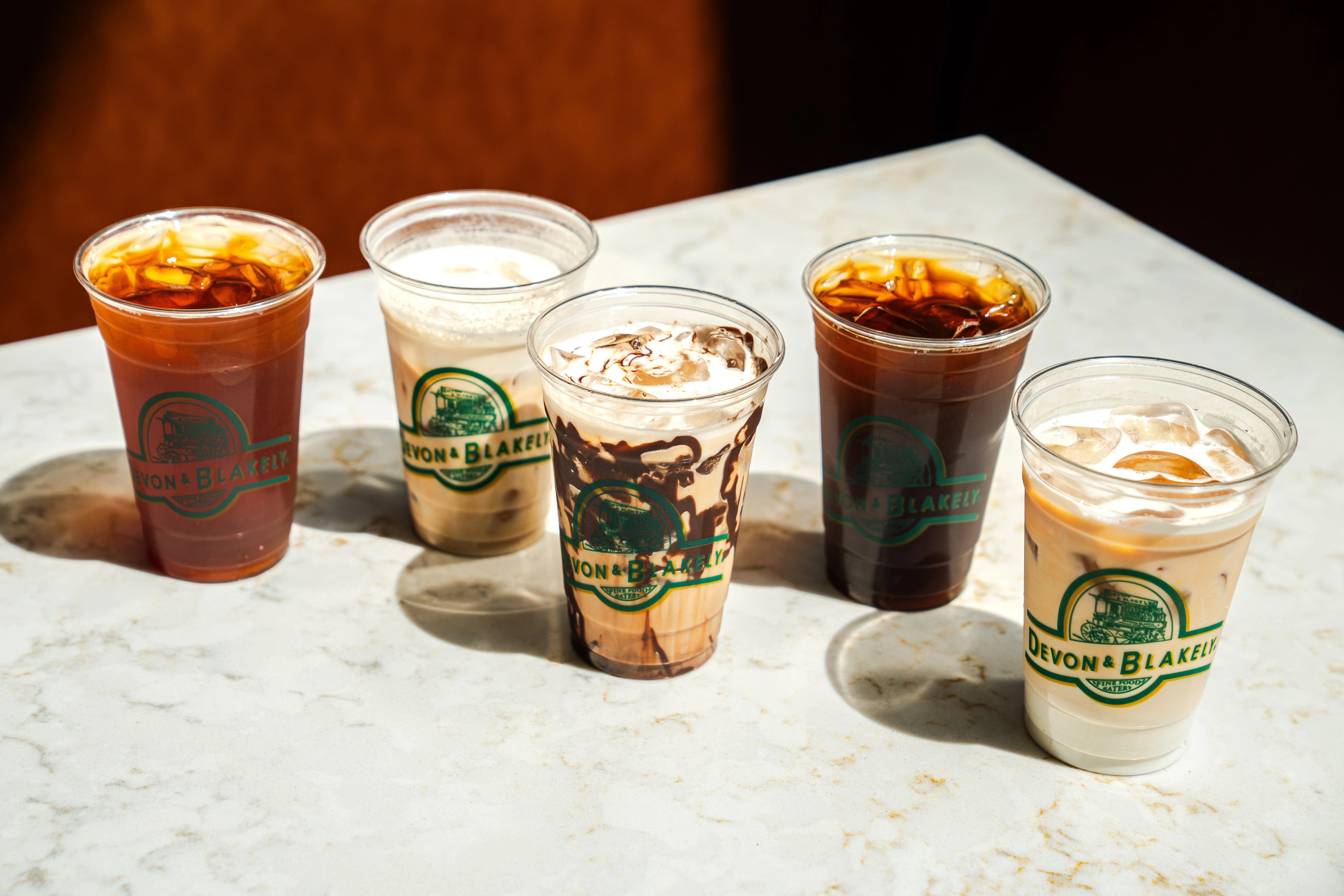 Five cups of iced coffee drinks, each with different colors and textures, arranged on a marble surface.