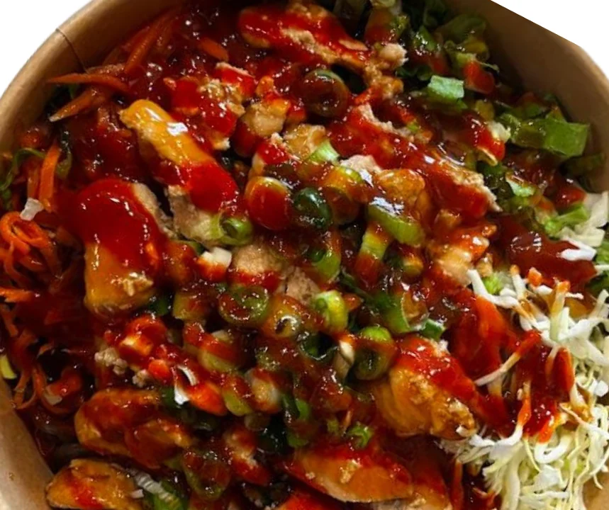 A bowl filled with shredded vegetables, chicken pieces, and a rich red sauce, garnished with green onions.