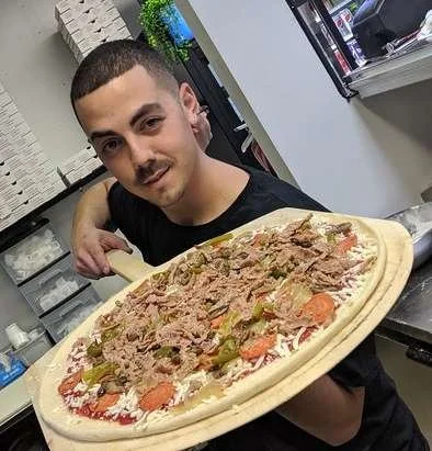 The owner of Lucino's Pizza about to put a pizza in the oven