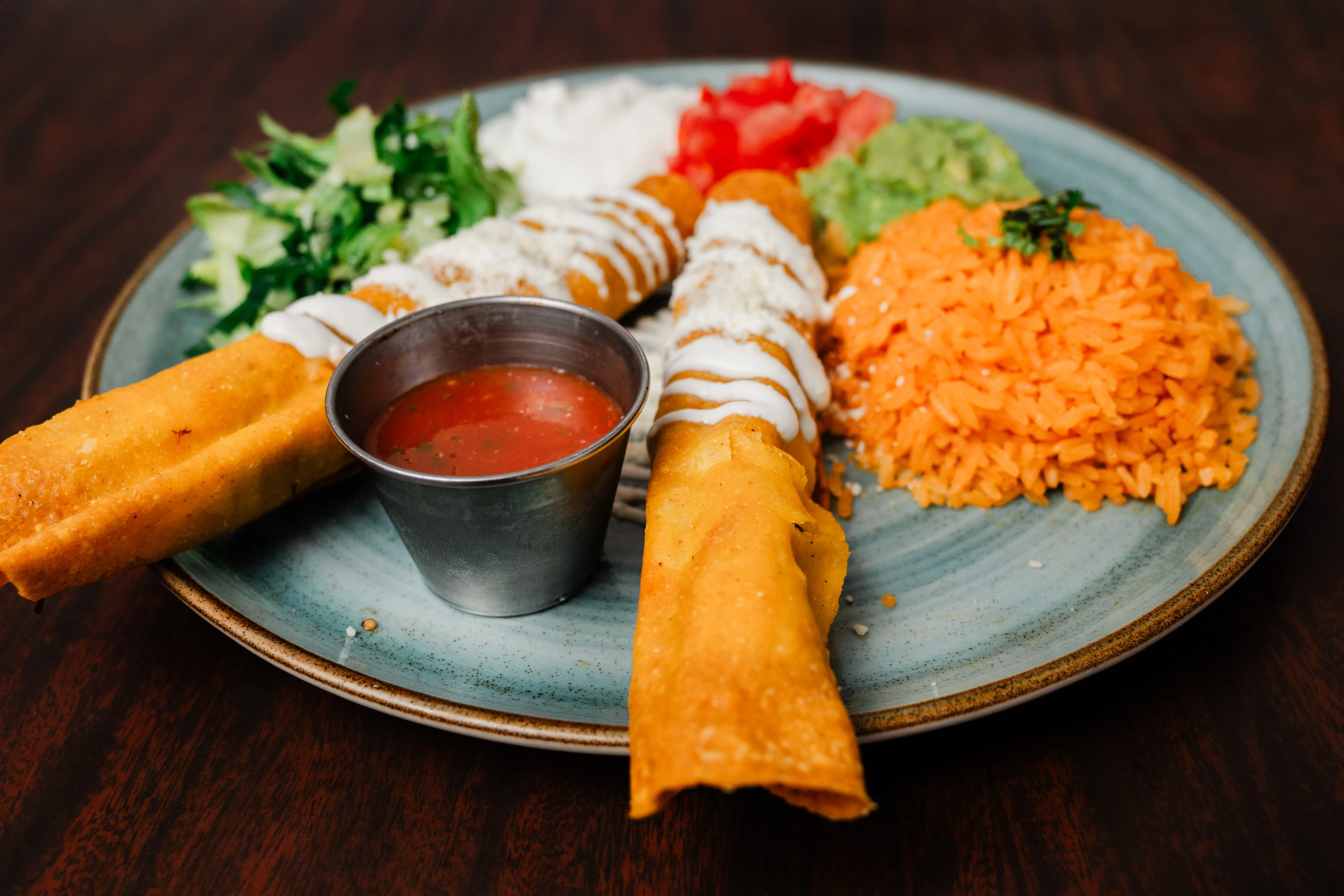 Plate of Mexican flautas with rice and fresh toppings