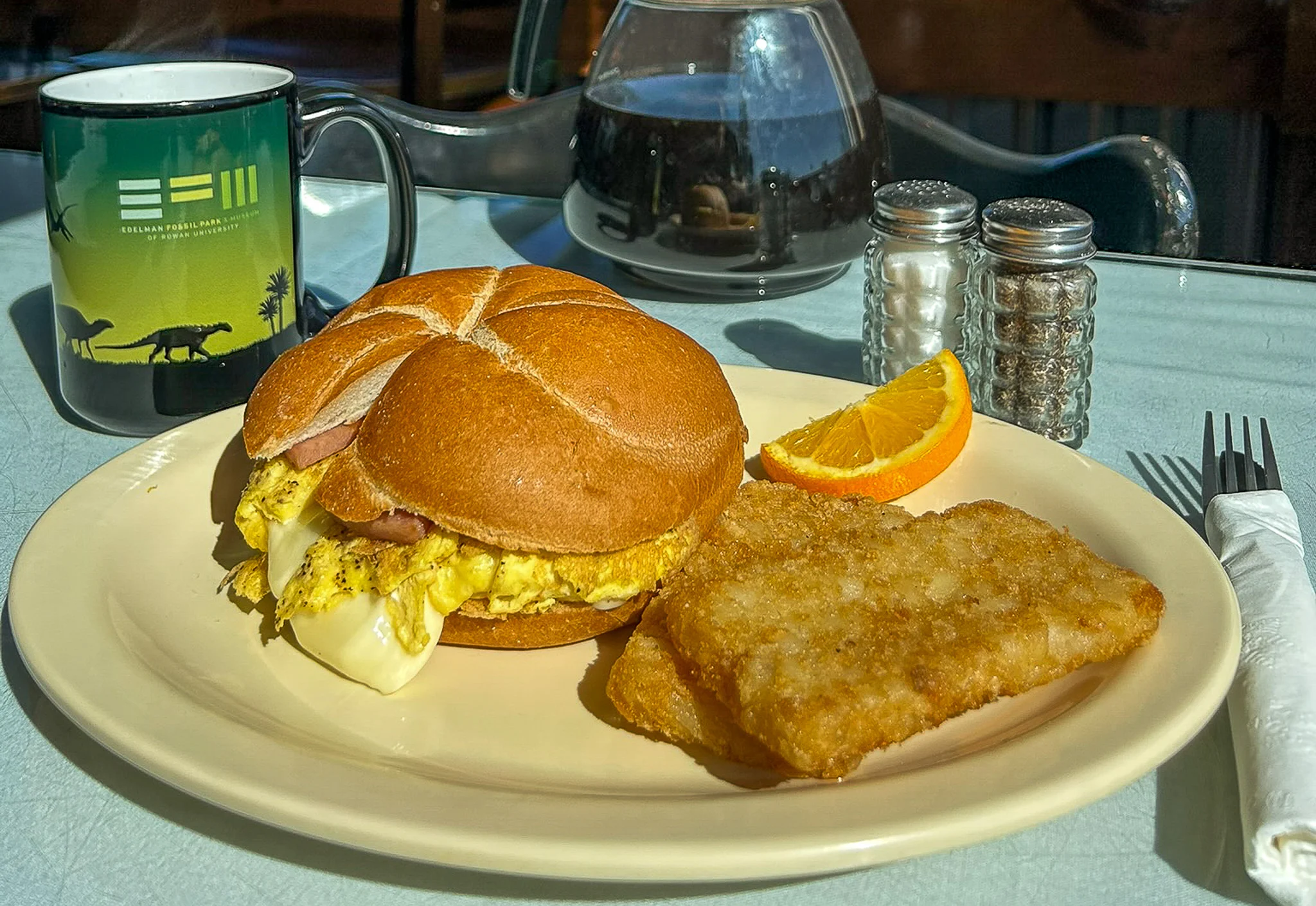 Golden hash brown and egg sandwich on a round roll served with orange slices and diner coffee setup