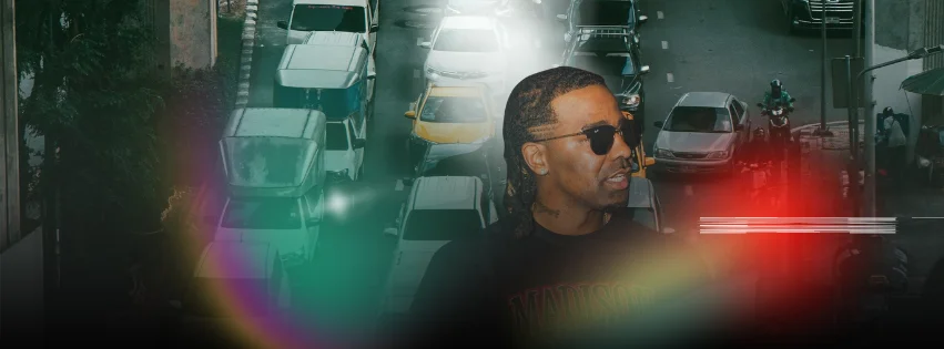 A stylish individual in sunglasses against a busy city traffic backdrop.