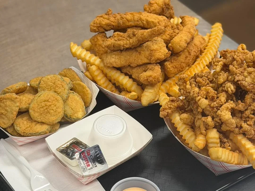 A tray featuring fried chicken tenders, French fries, and fried pickles, accompanied by dipping sauces.