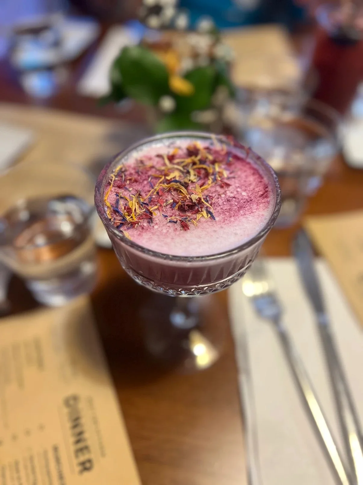 A beautifully presented drink with a frothy top, garnished with dried flowers, served in an ornate glass.