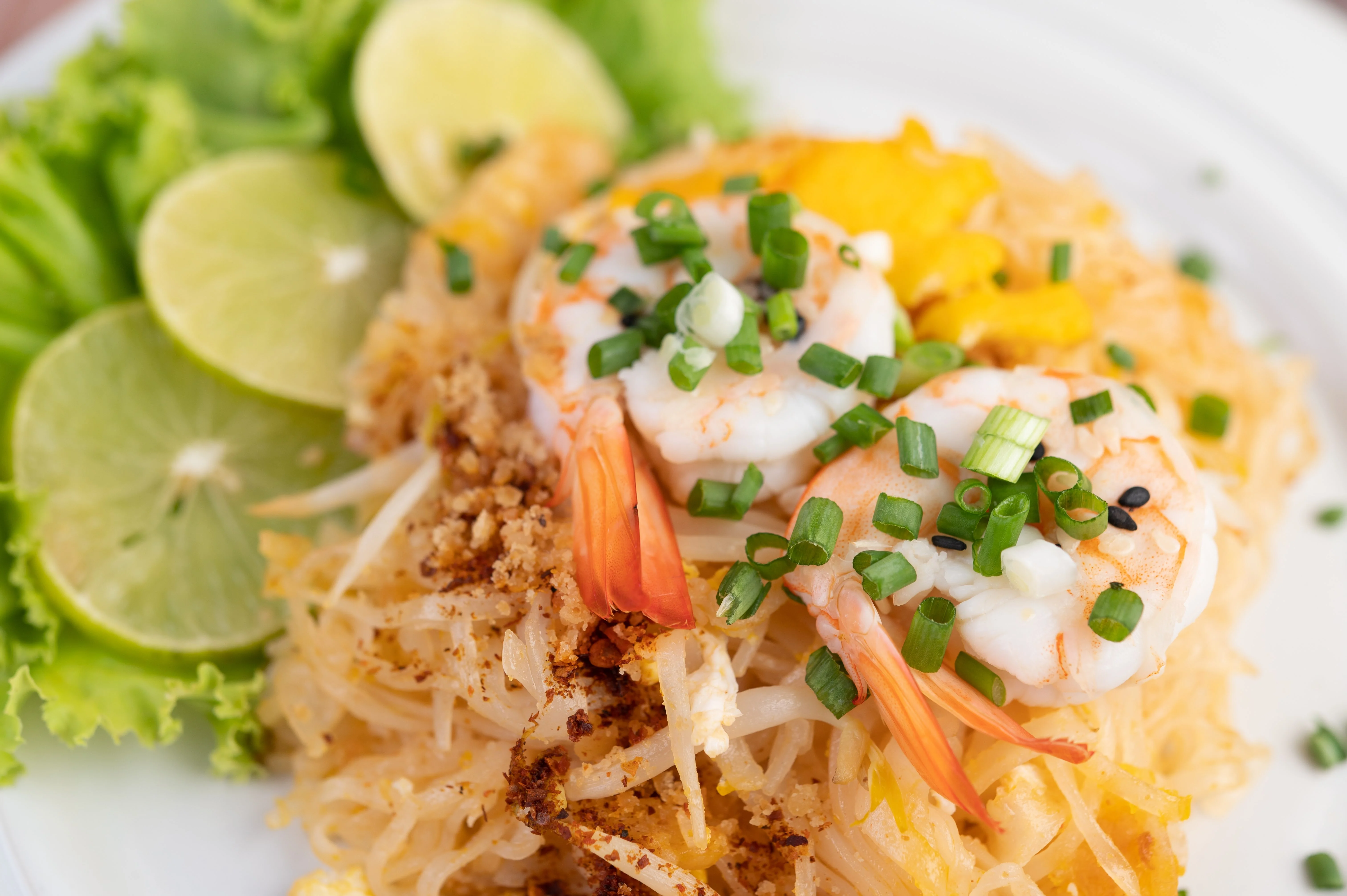 Plate of fresh shrimp pad thai garnished with lime and herbs
