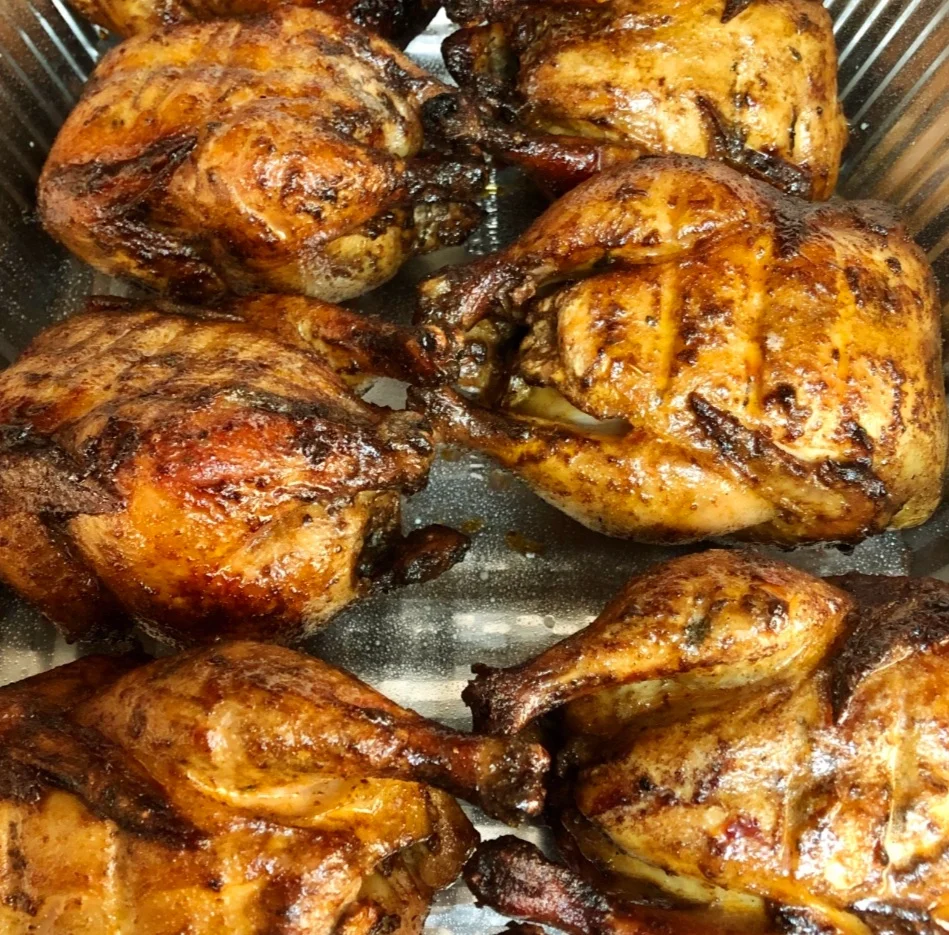 A tray filled with several golden-brown, grilled chickens, showcasing a crispy skin and juicy appearance.