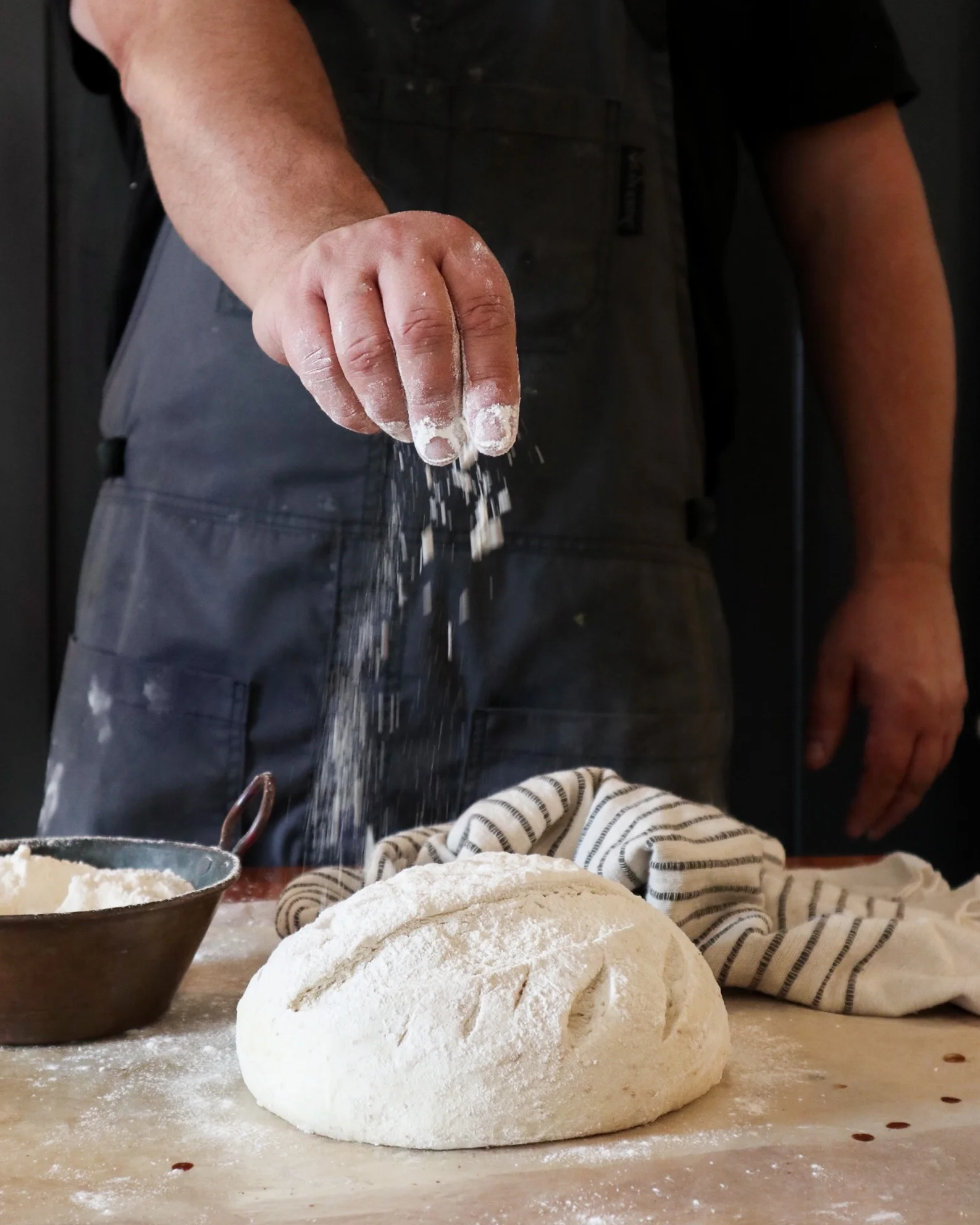 Baker sprinkling flour over artisan bread dough
