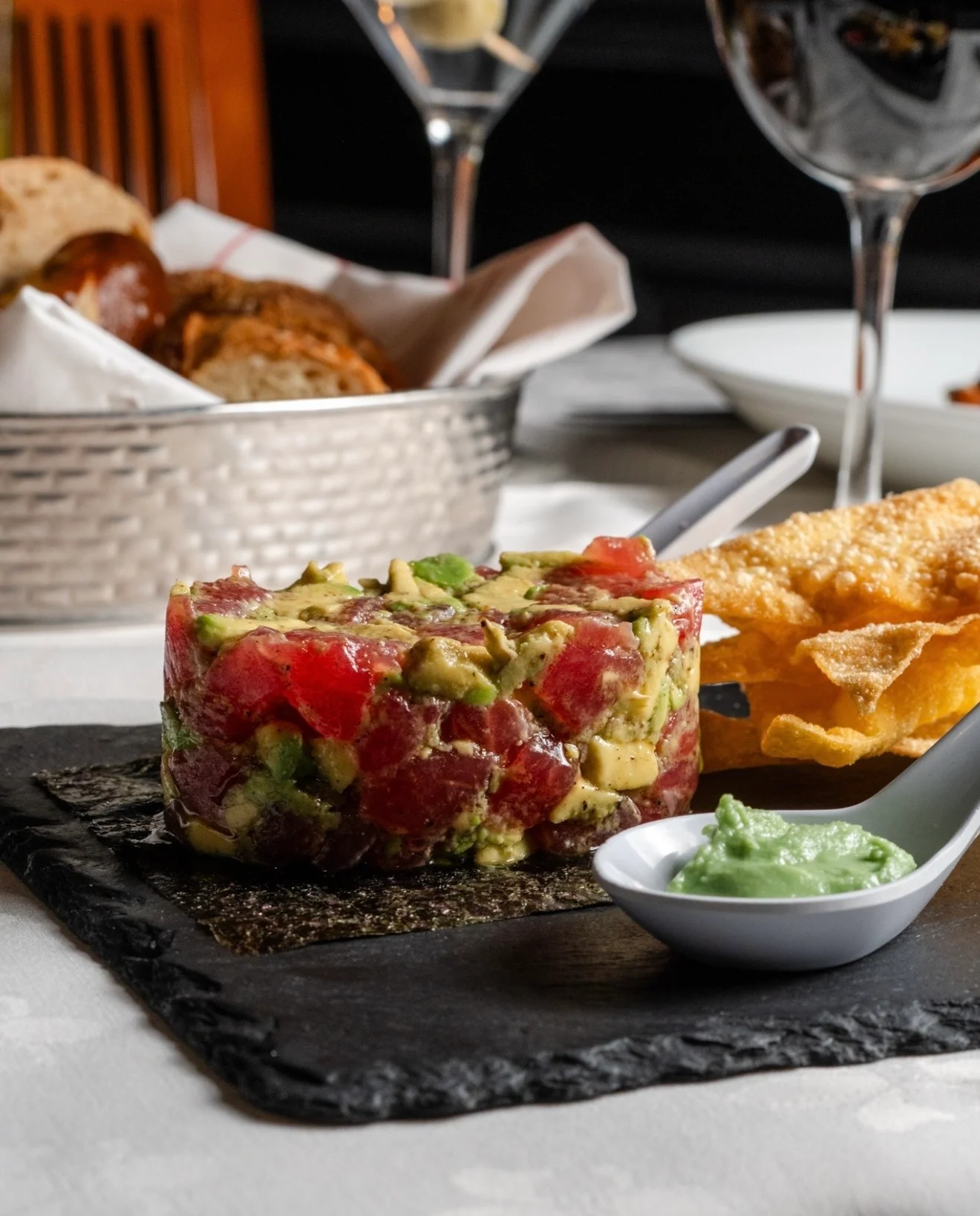 A colorful tuna tartare dish mixed with avocado, served with crunchy chips and a green sauce.