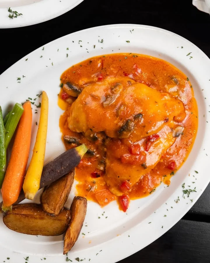 A savory dish featuring chicken in a rich sauce, served alongside colorful vegetables including carrots and potatoes.