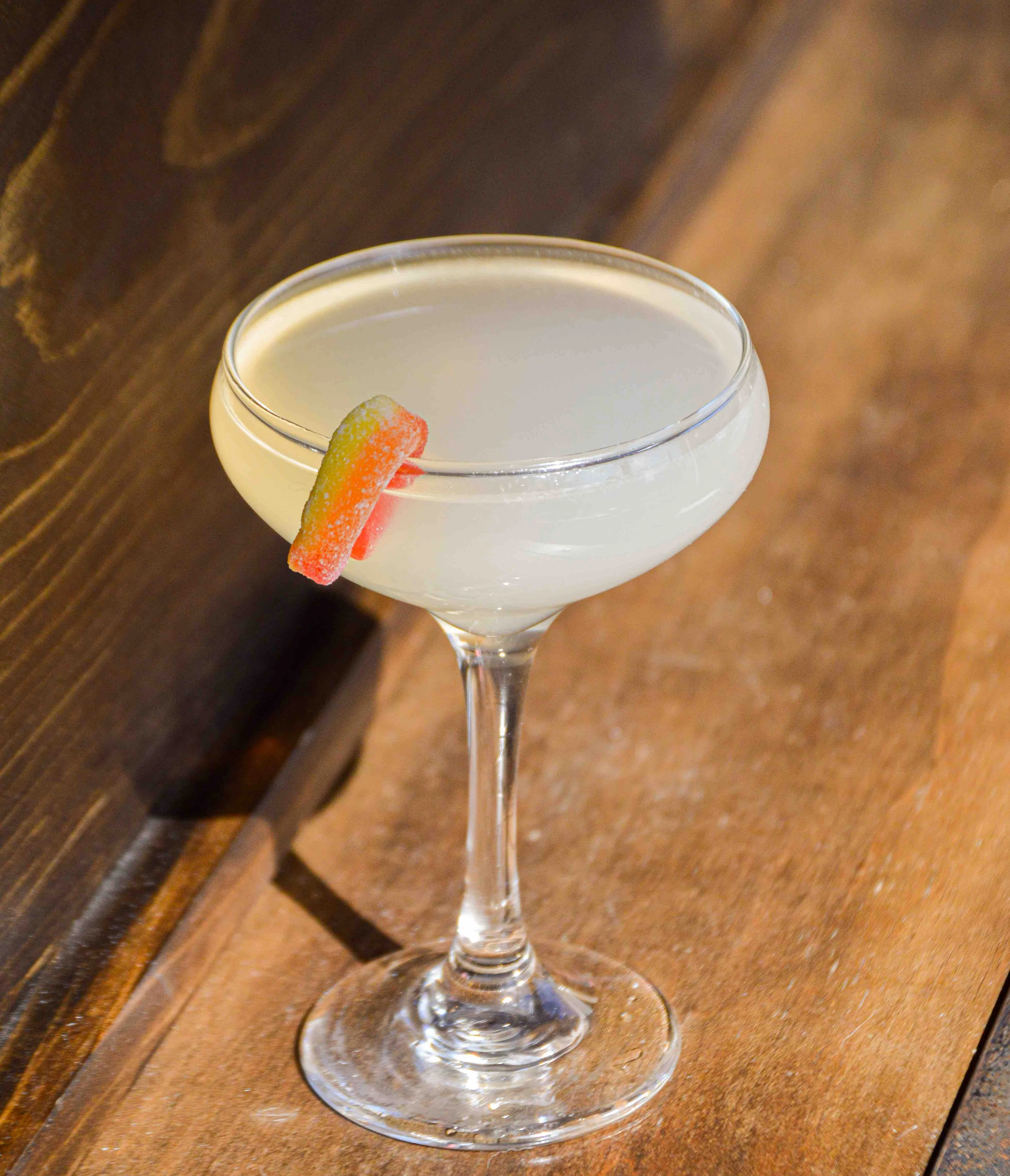 Just Peachy cocktail sitting on a wooden table, garnished with a peach ring