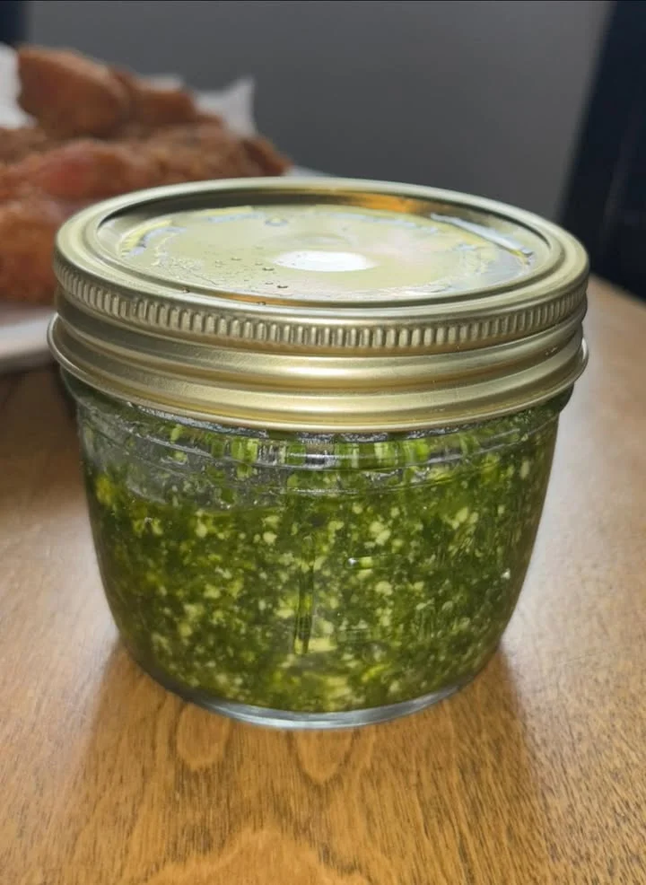 A jar filled with homemade green pesto sauce, sitting on a wooden surface.