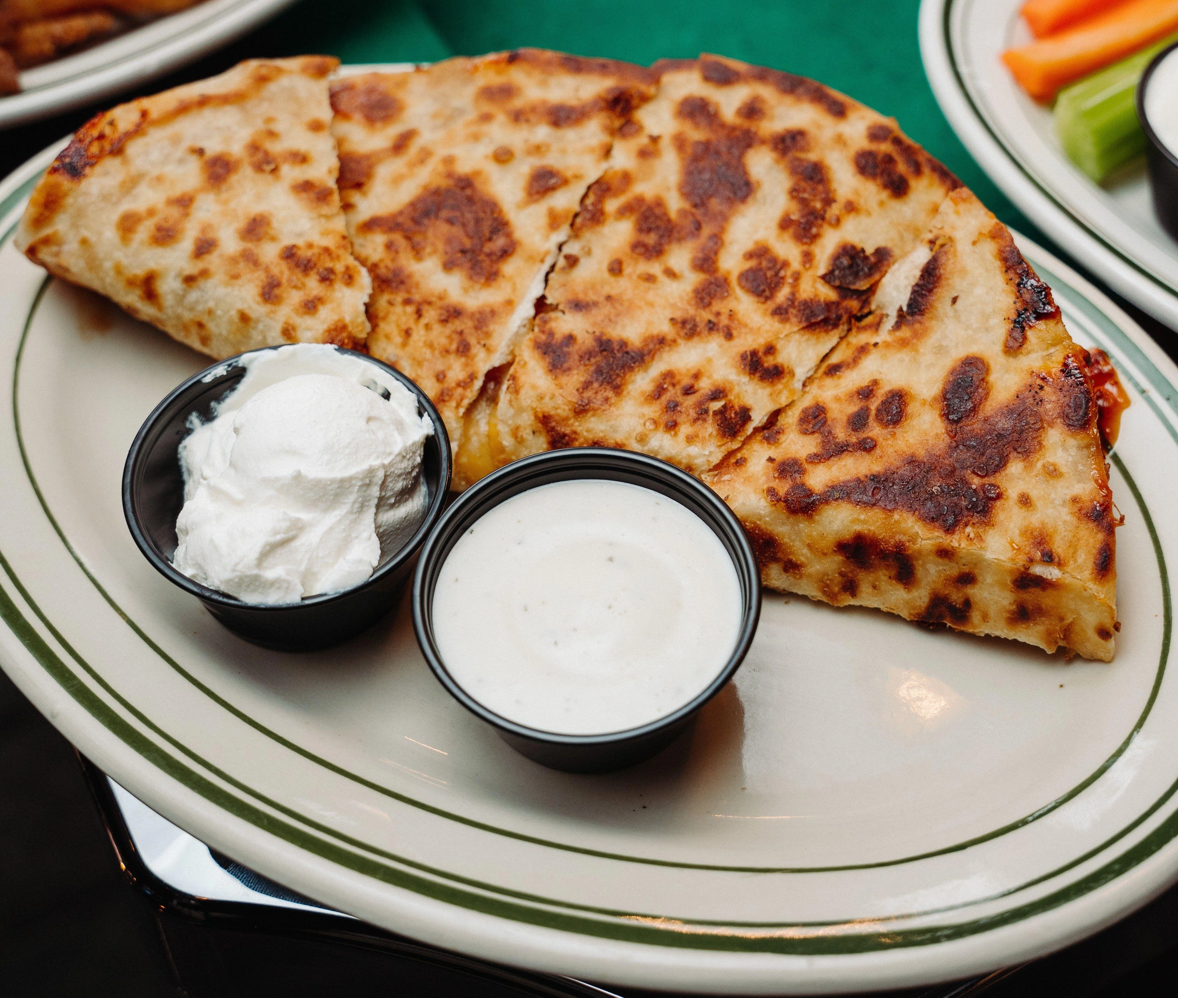 A plate of quesadillas cut into wedges, served with two dipping sauces: one creamy and one ranch-style.