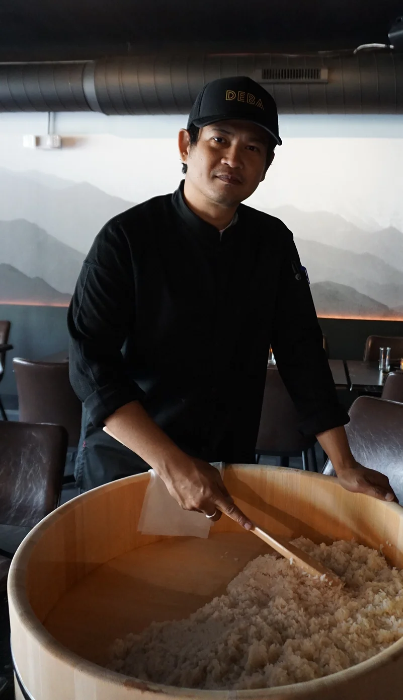 Chef preparing rice in a wooden tub at a modern restaurant.