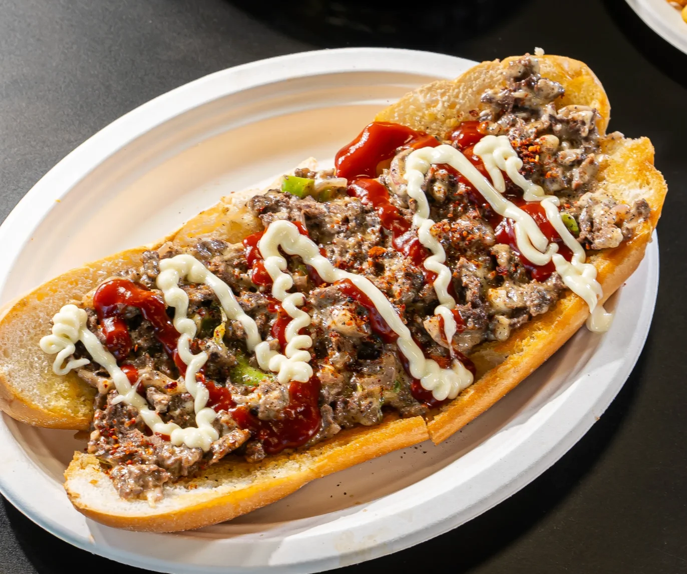 A sandwich loaded with a chunky meat filling, garnished with ketchup and mayonnaise on a toasted bun.