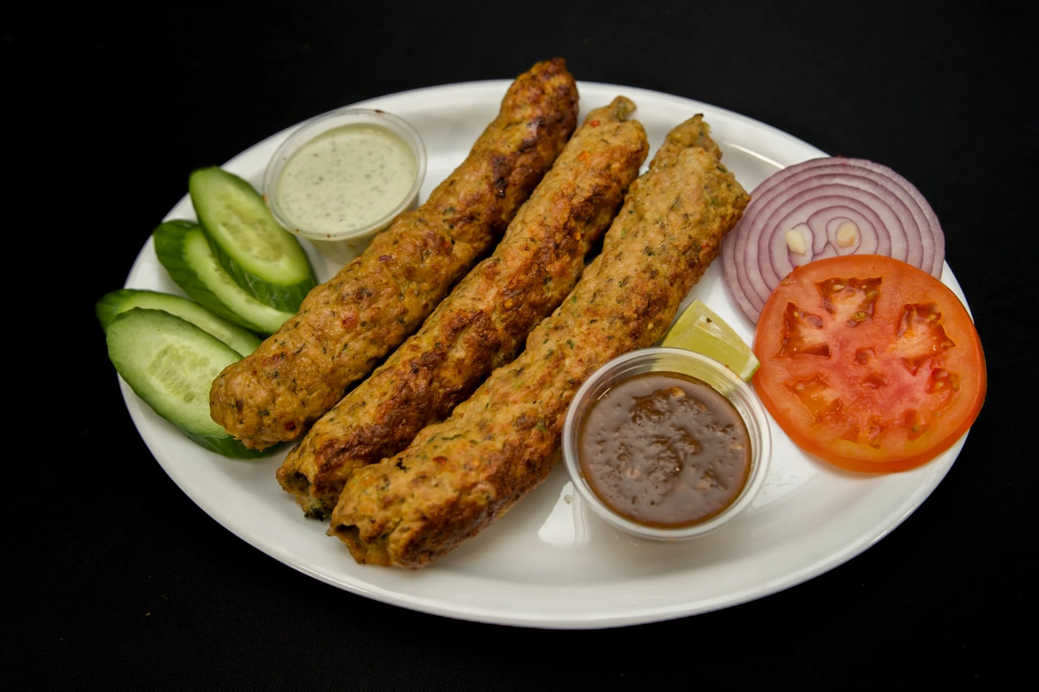 Grilled seekh kebabs served with mint raita, tamarind chutney, and fresh salad at Karachi BBQ Tonight.
