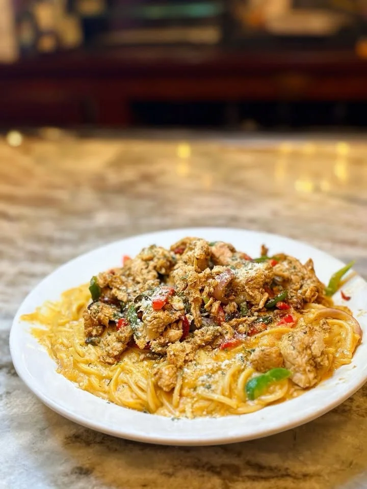 A serving of spaghetti topped with a rich, flavorful sauce and mixed vegetables. The dish is garnished and served on a white plate.