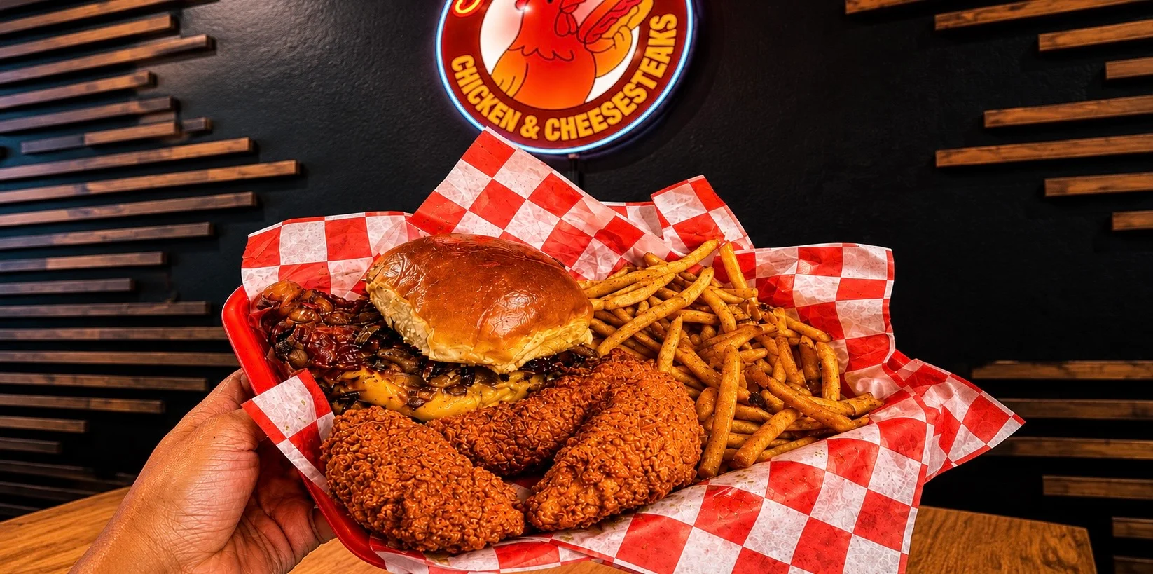 A basket containing a sandwich, fried chicken pieces, and a side of fries, presented on red and white checkered paper.