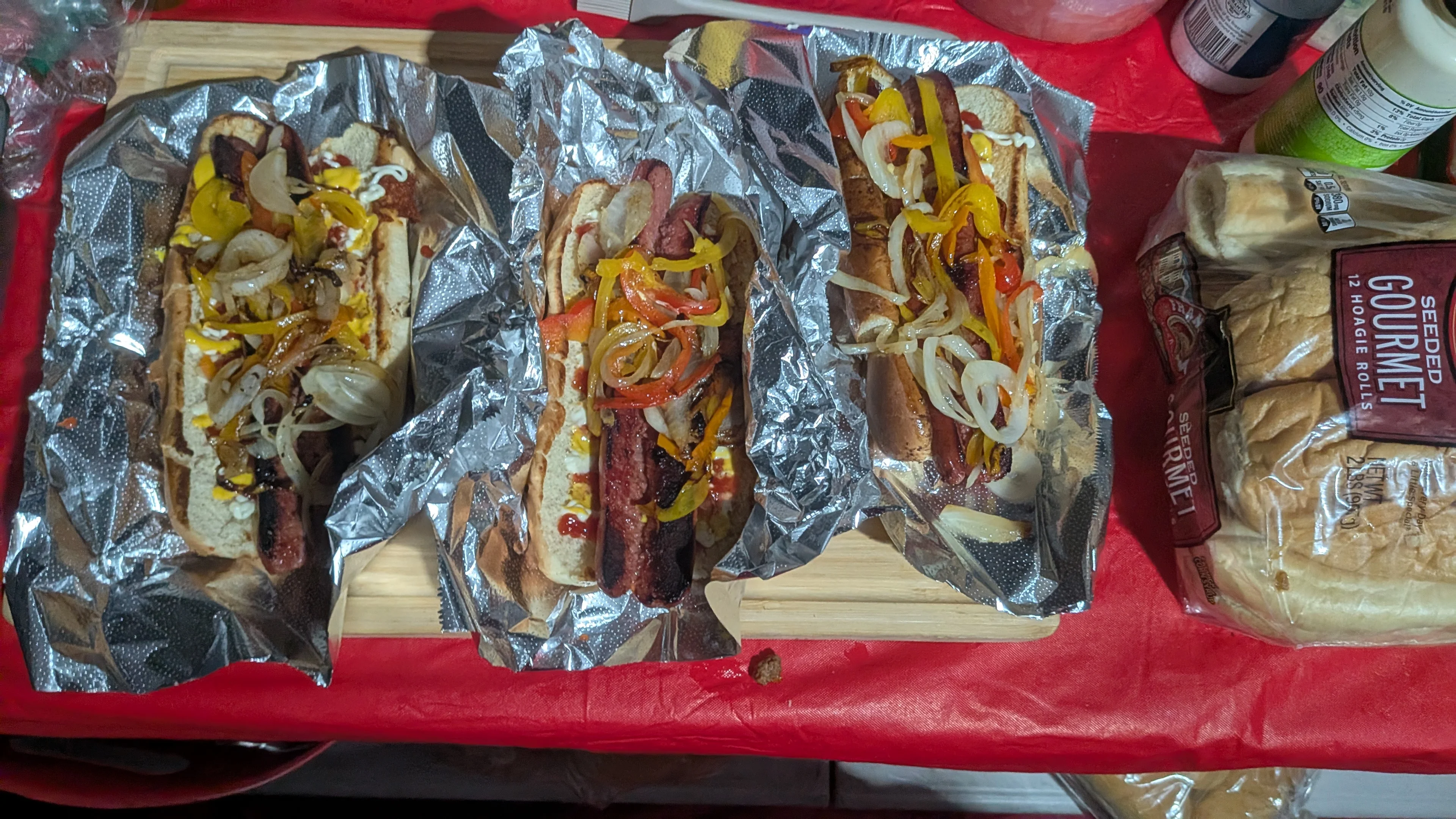 Three loaded hot dogs topped with various condiments and fried onions, wrapped in foil.