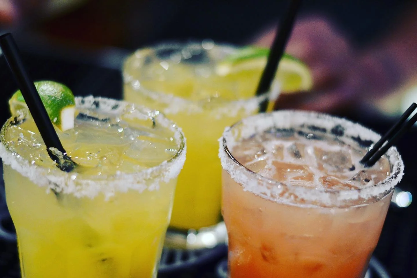 Three colorful margaritas with salted rims on a table at a Mexican restaurant.