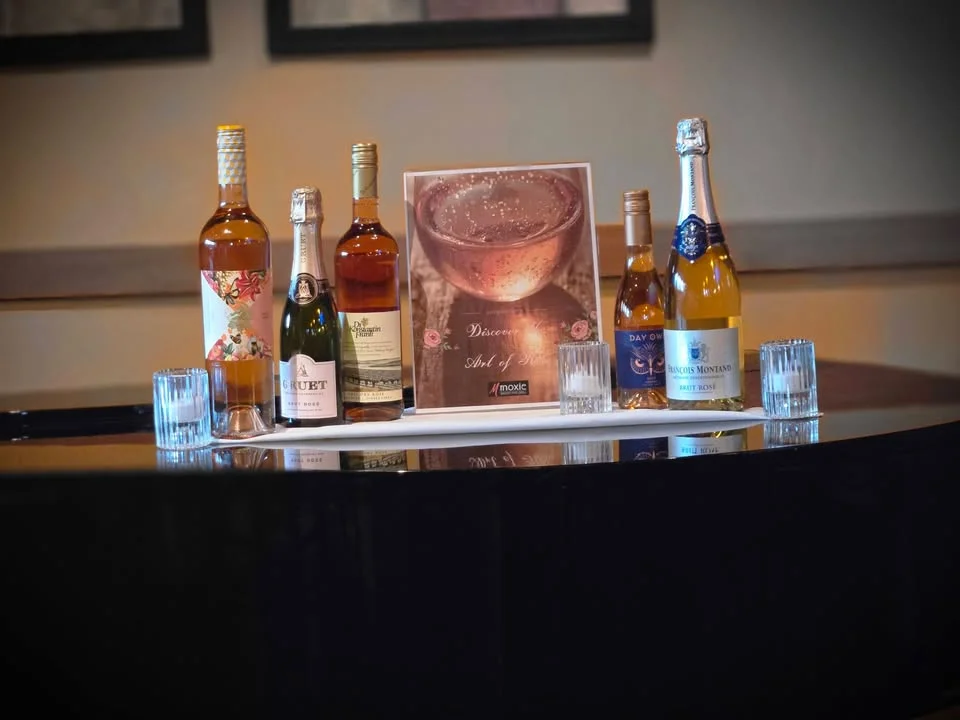 An assortment of wine bottles elegantly displayed with a promotional sign. The setting features decorative glasses and a focus on a polished surface.