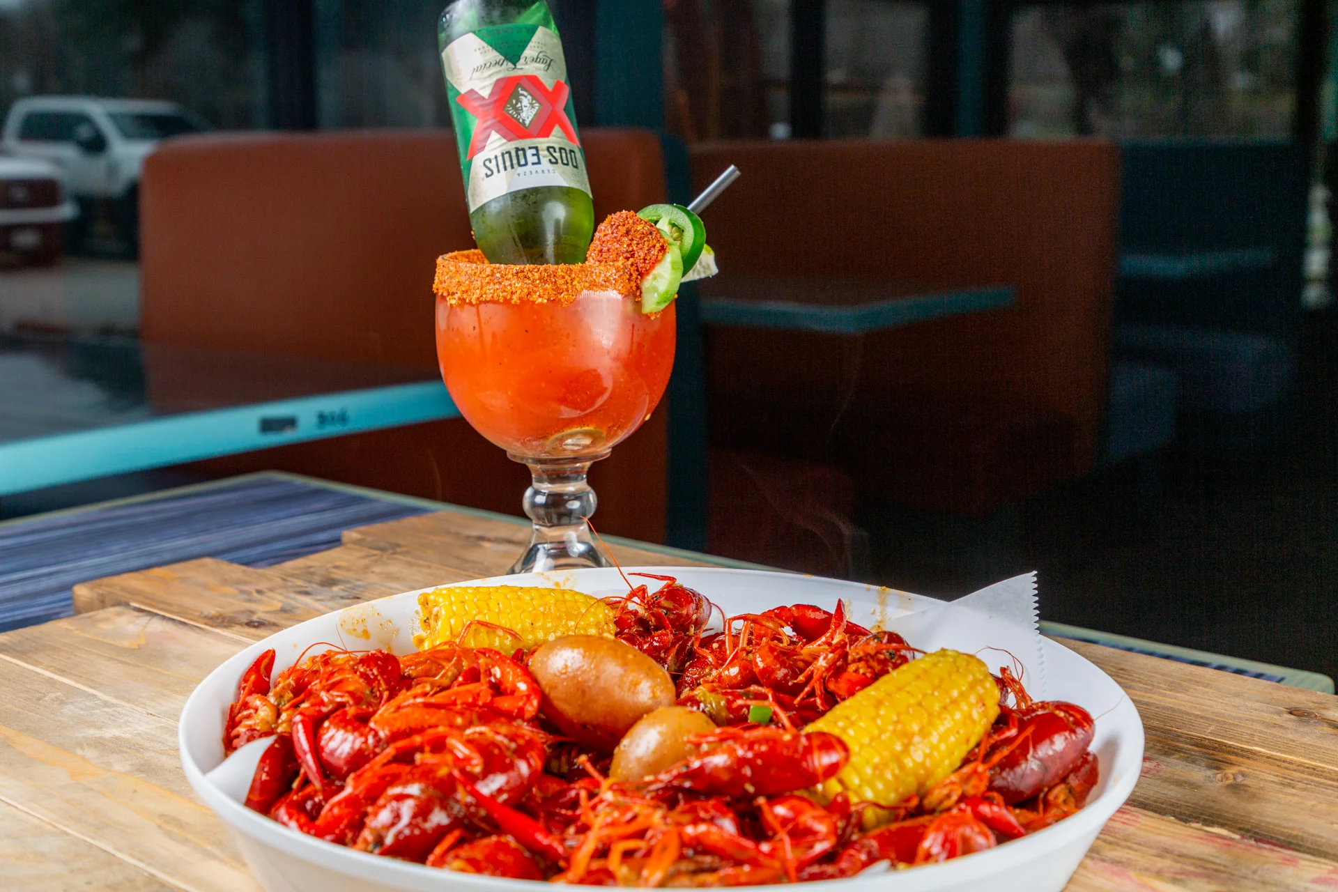 A vibrant platter of crawfish surrounded by corn and potatoes, paired with a large cocktail topped with a beer.