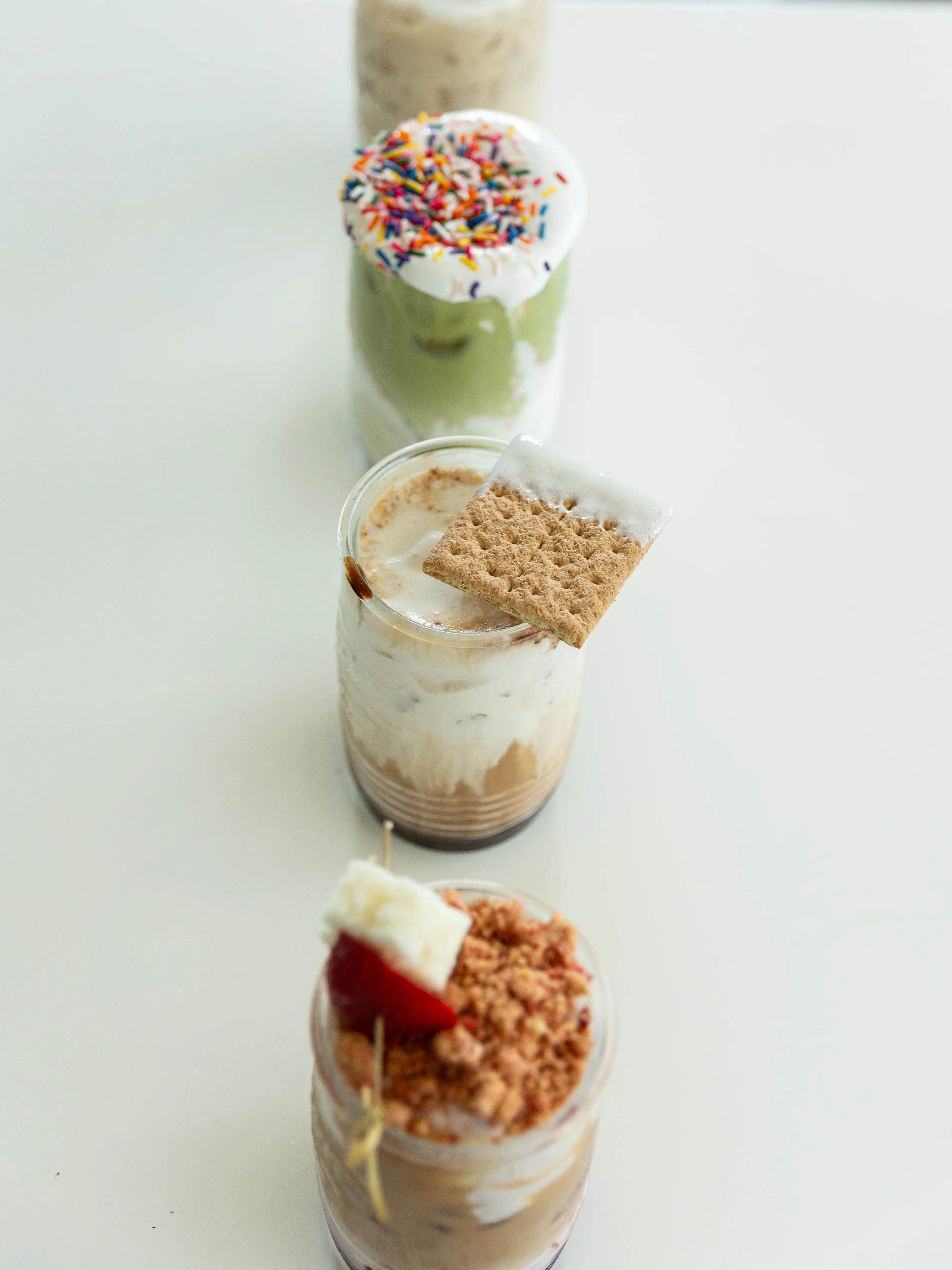 A lineup of delectable desserts in jars, featuring various layers and toppings, including sprinkles and cookies, creating a colorful and enticing display.