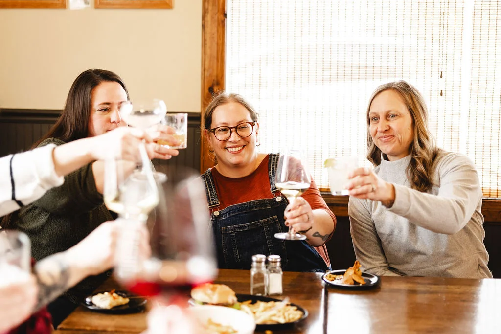 A group of friends toasting with drinks at a table filled with food, showcasing a lively and celebratory atmosphere.