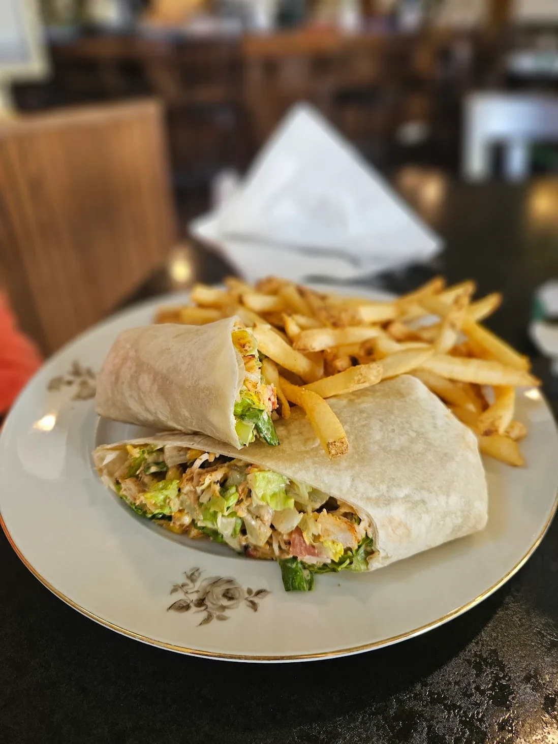 A plate with a wrapped burrito and a side of French fries.