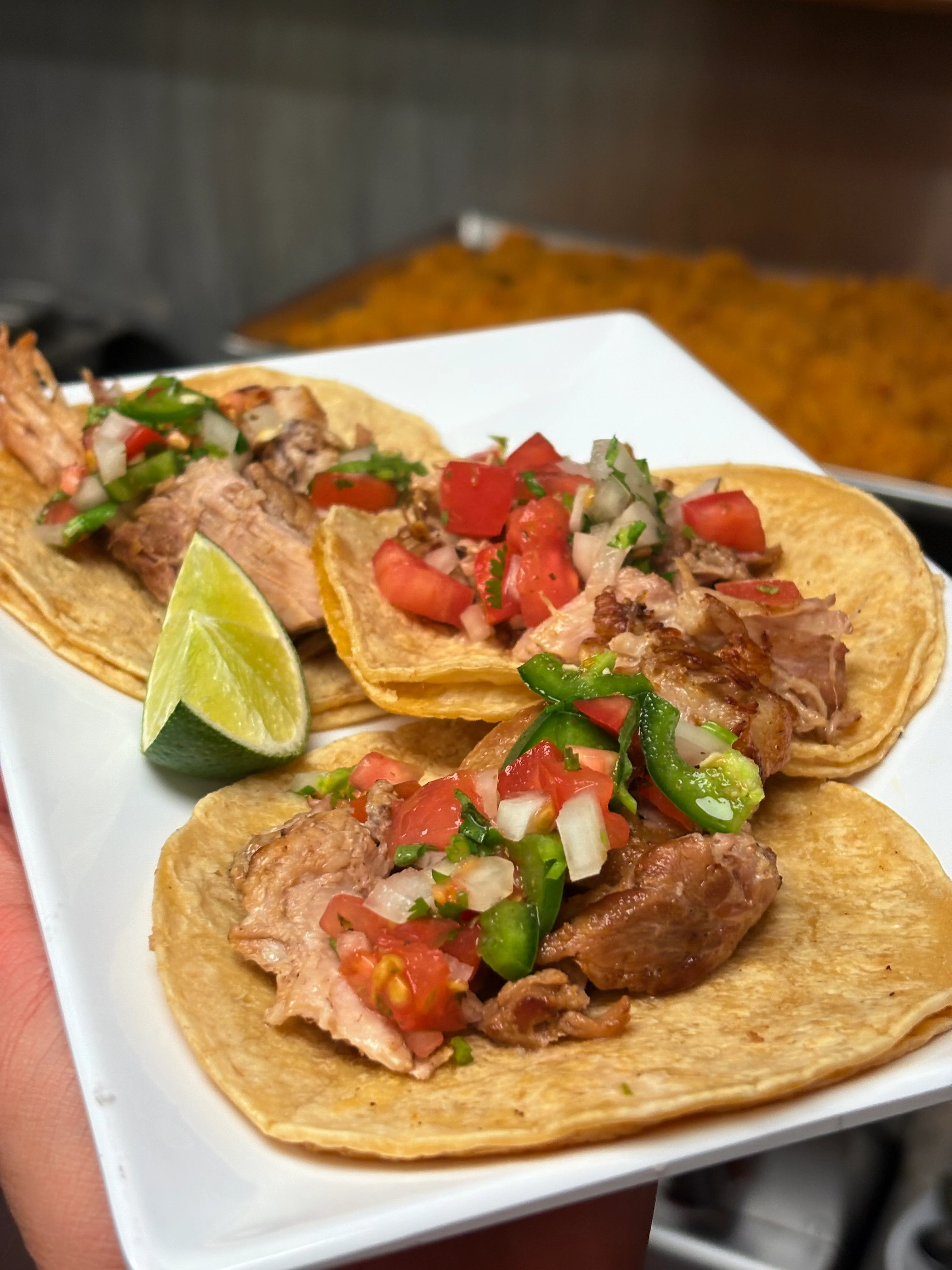 Three tacos filled with tender meat, topped with fresh pico de gallo and cilantro, served with a lime wedge on a white plate.