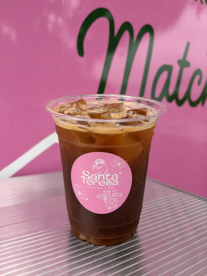A glass of iced coffee with ice cubes, served in a clear cup with a prominent logo.