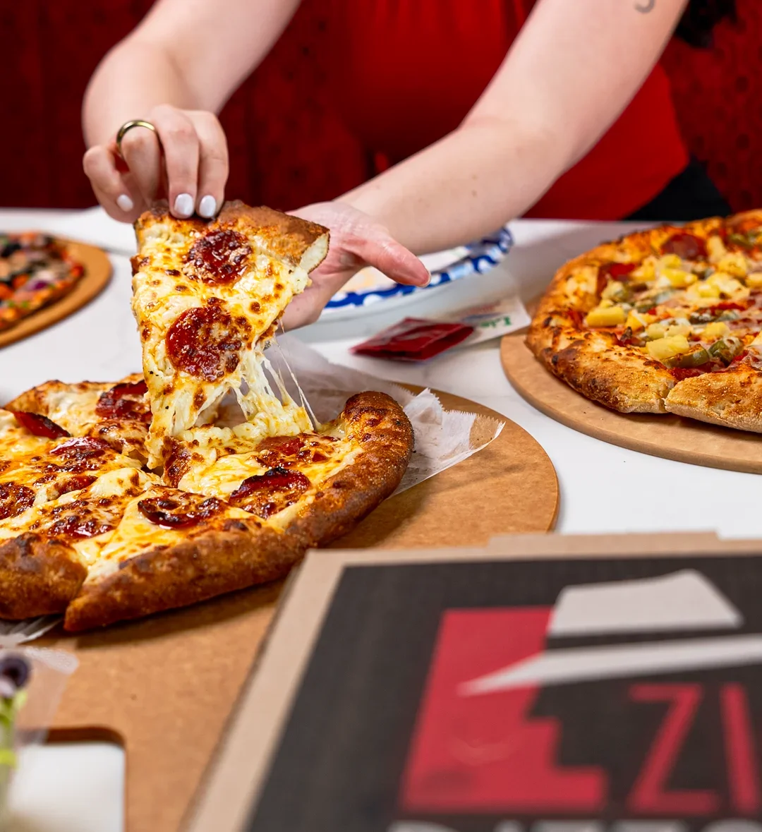 A hand reaching for a slice of pepperoni pizza with melted cheese.