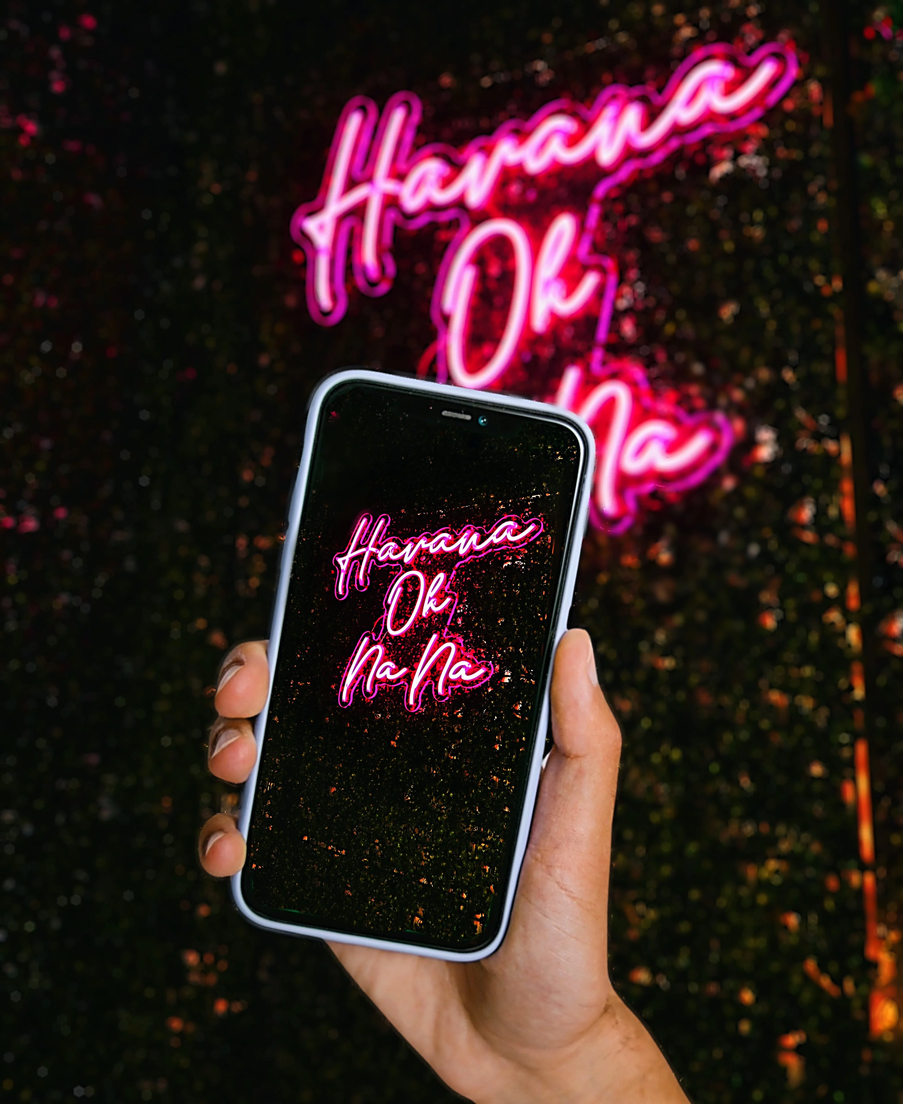 Hand holding a smartphone displaying neon sign 'Havana Oh Na Na'