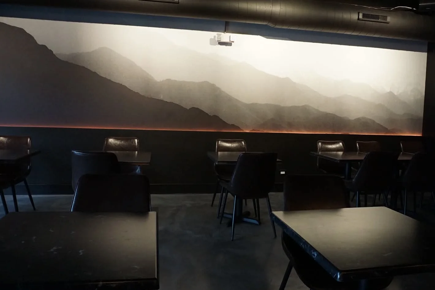 Modern restaurant interior with mountain mural and dark furniture.
