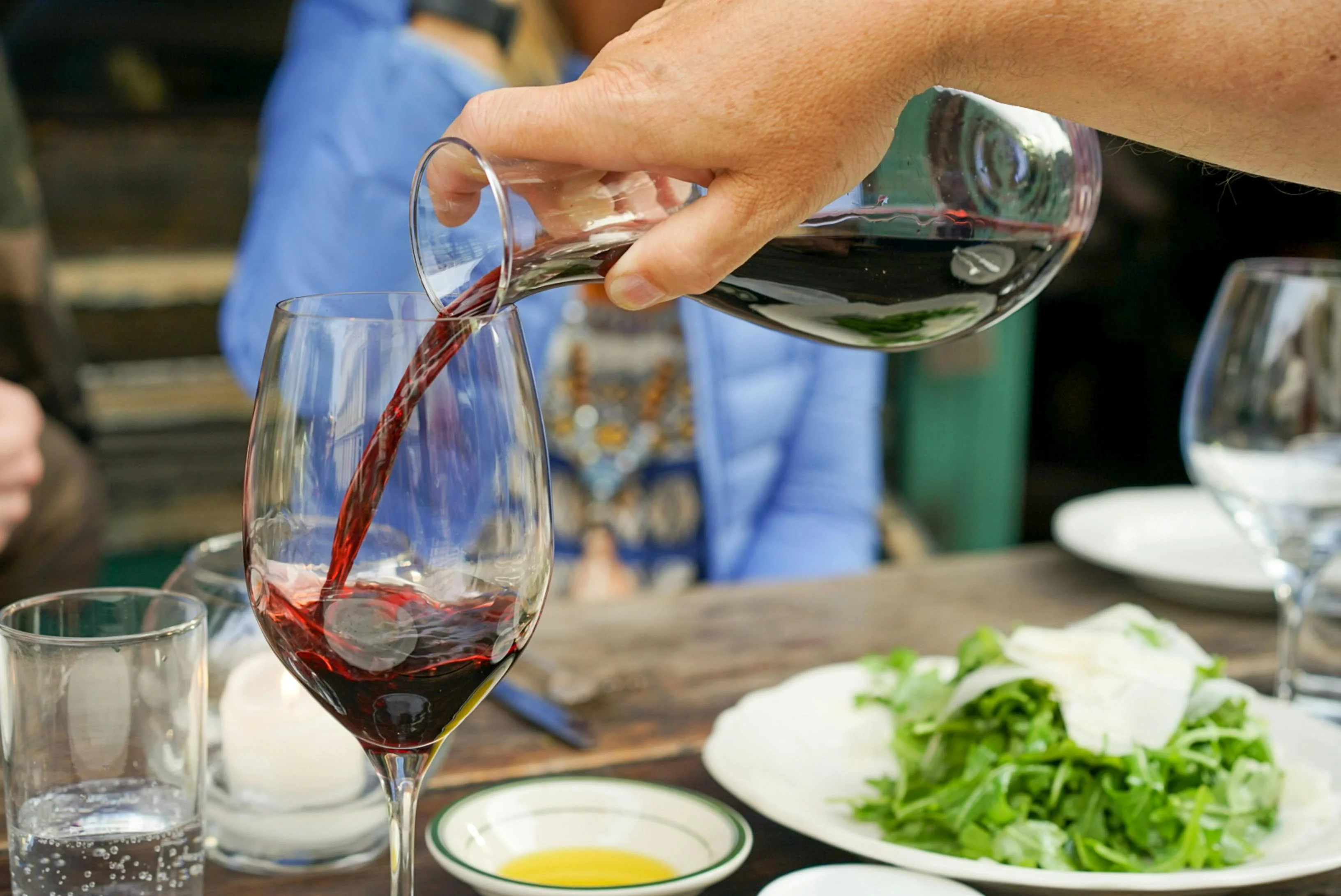 Pouring red wine into a glass at a dining table with fresh salad.
