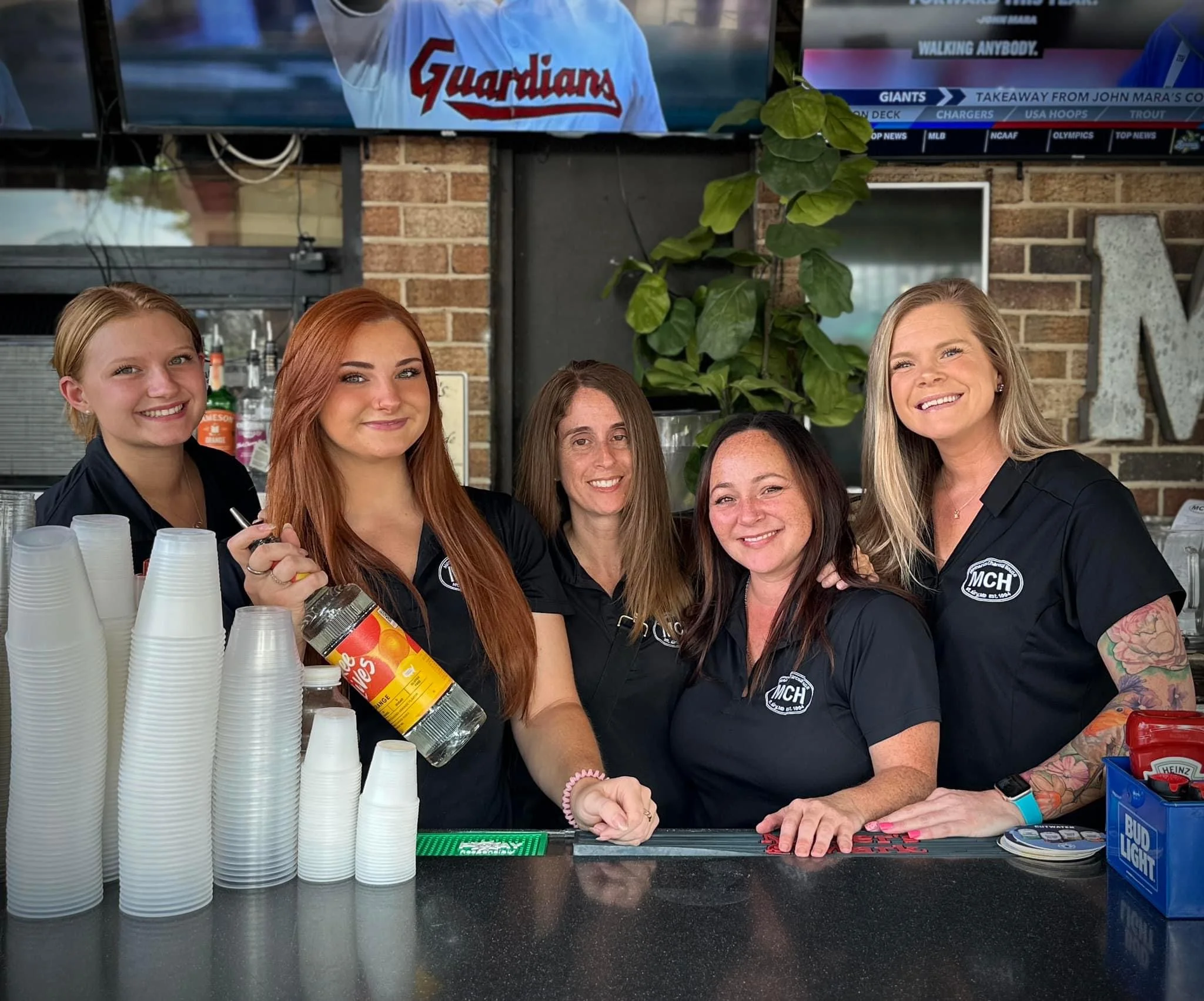 Bartenders smiling behind a bar counter with drinks and cups