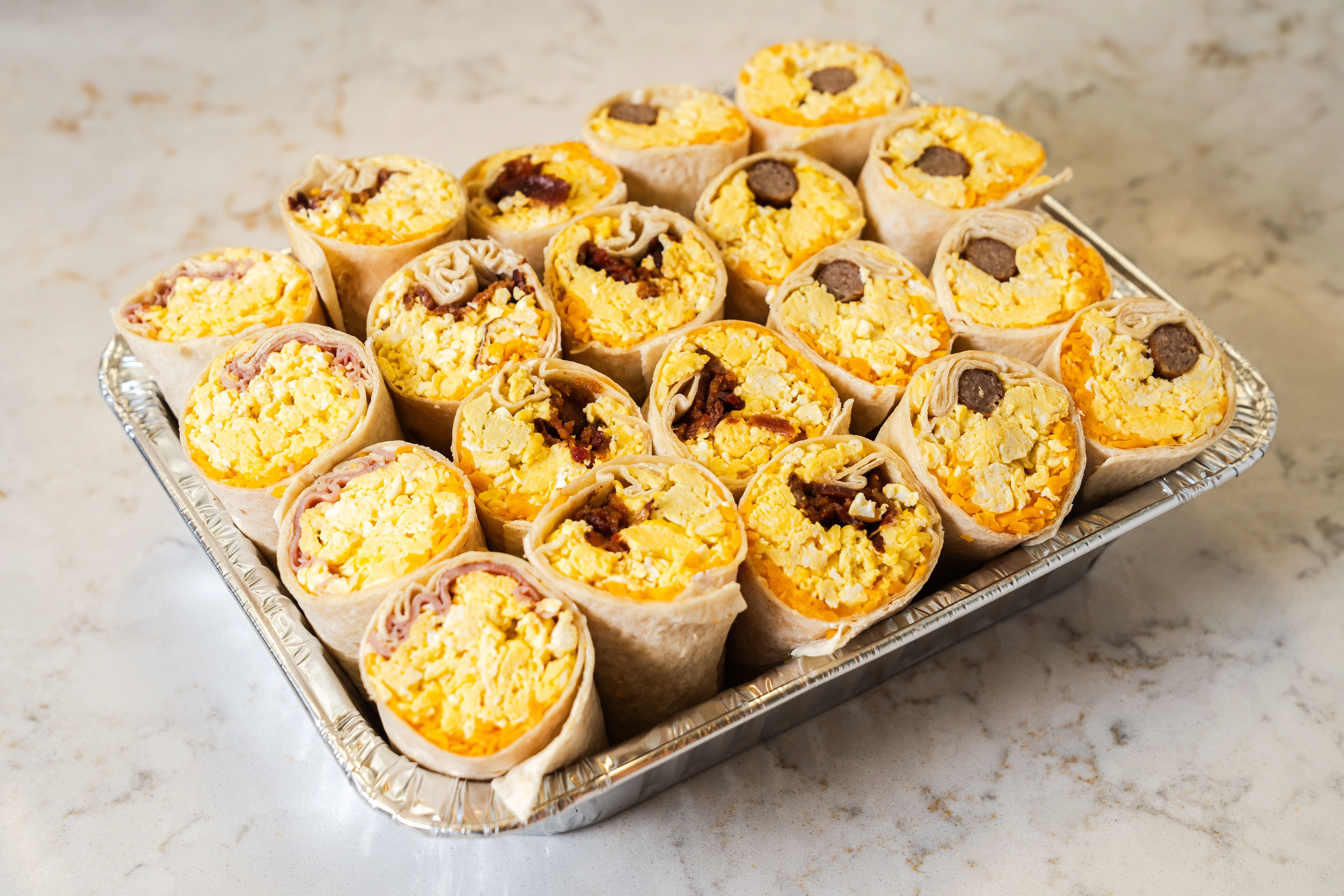 A tray of rolled breakfast burritos with various fillings.