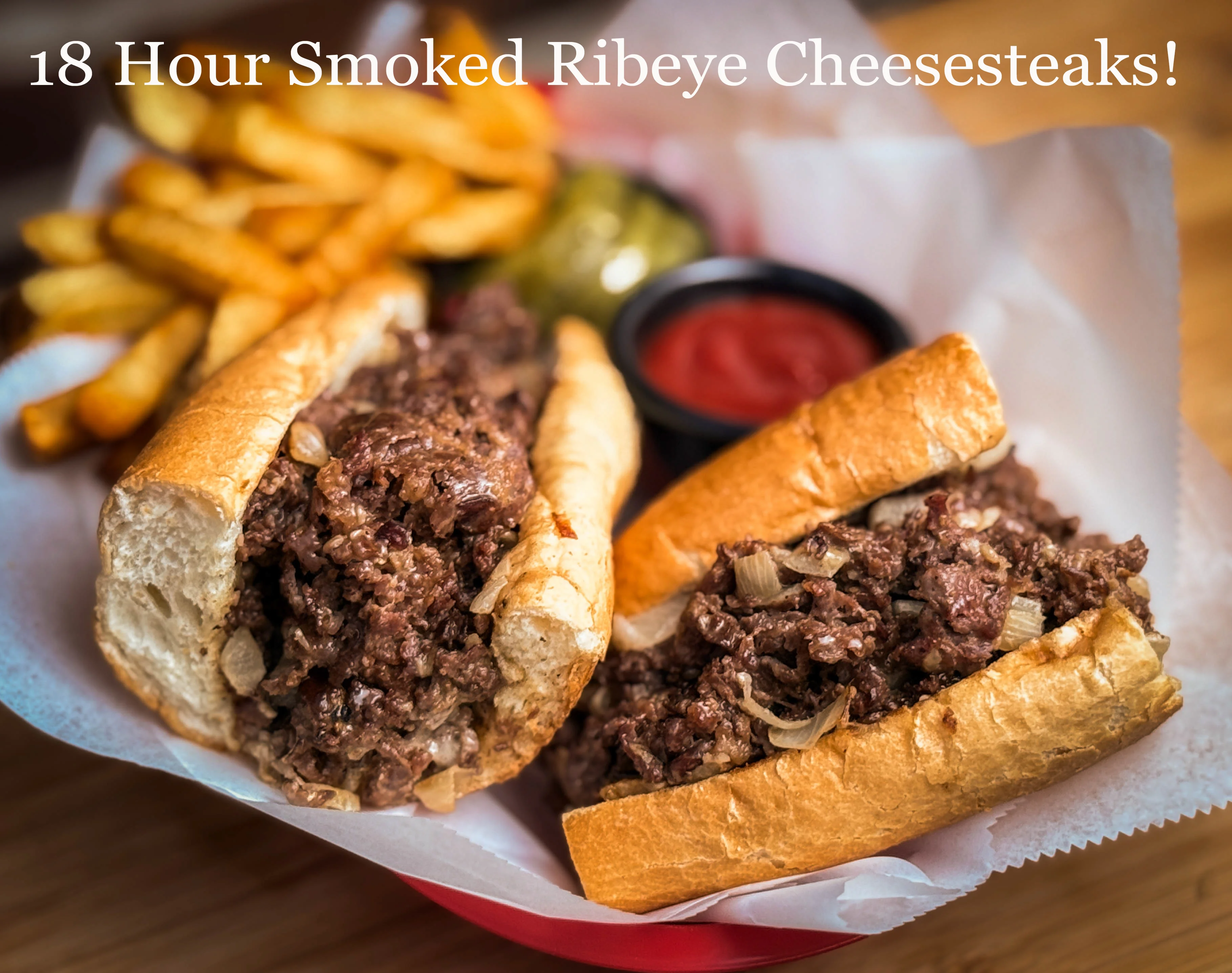 A delicious serving of two cheesesteak sandwiches filled with smoked ribeye, onions, and served with fries on the side.