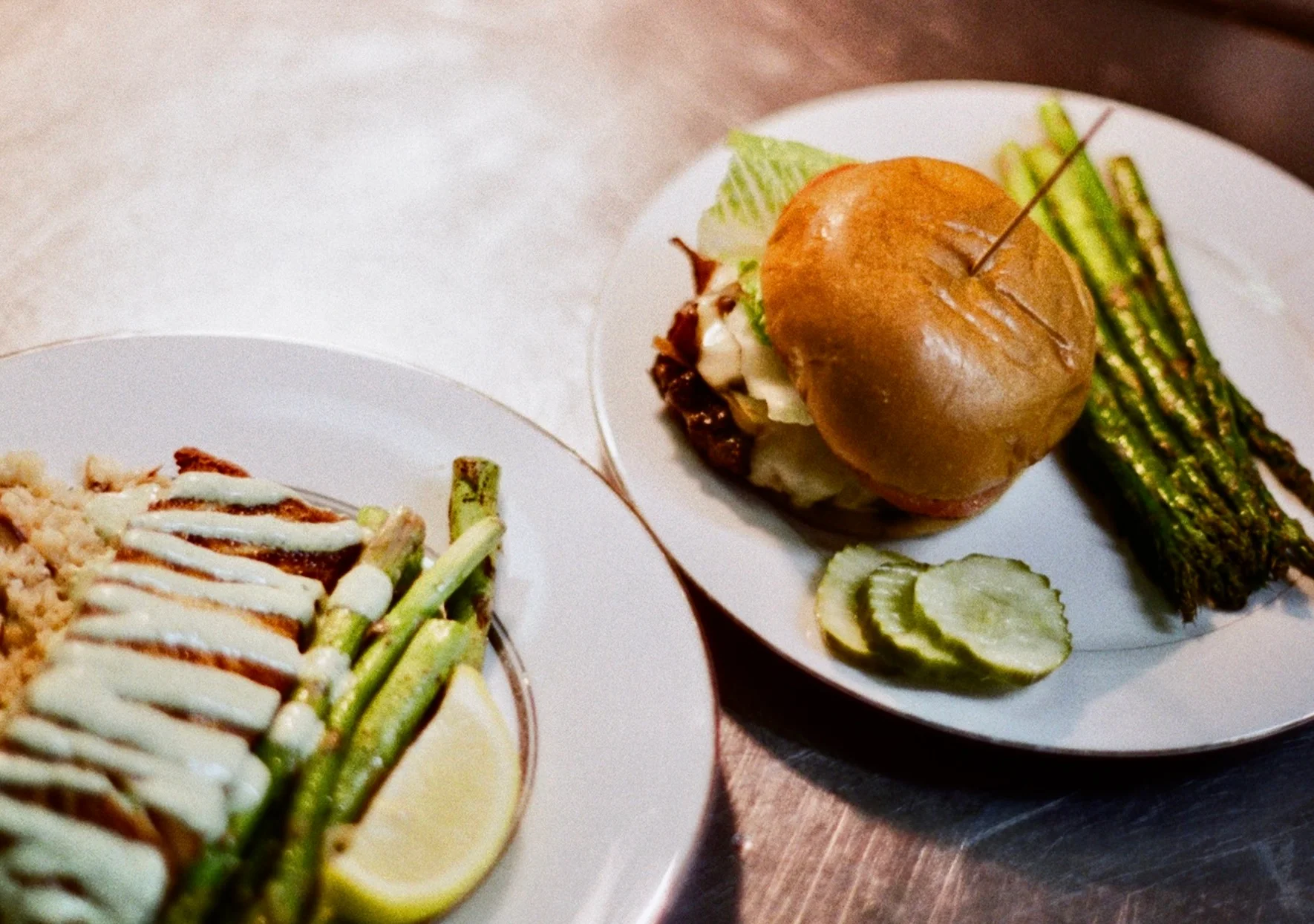 A delicious meal featuring grilled chicken, asparagus, and a sandwich, presented on stylish plates.