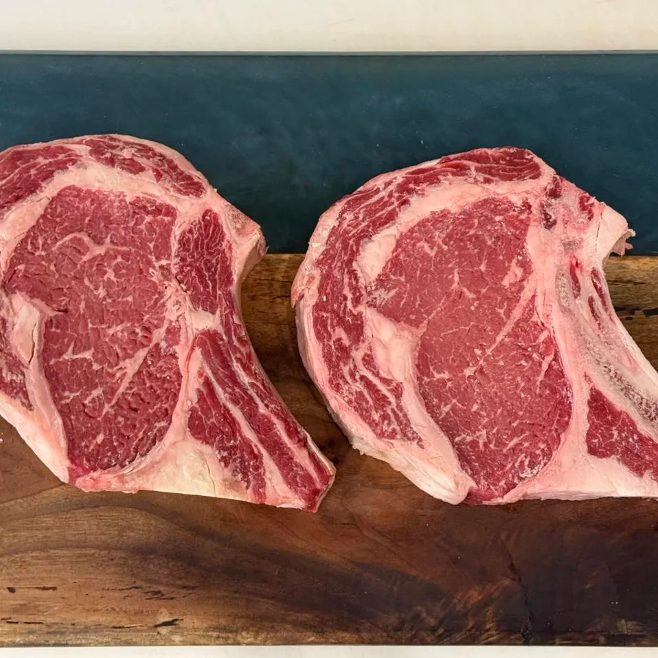 Two beautifully marbled tomahawk steaks on a wooden cutting board