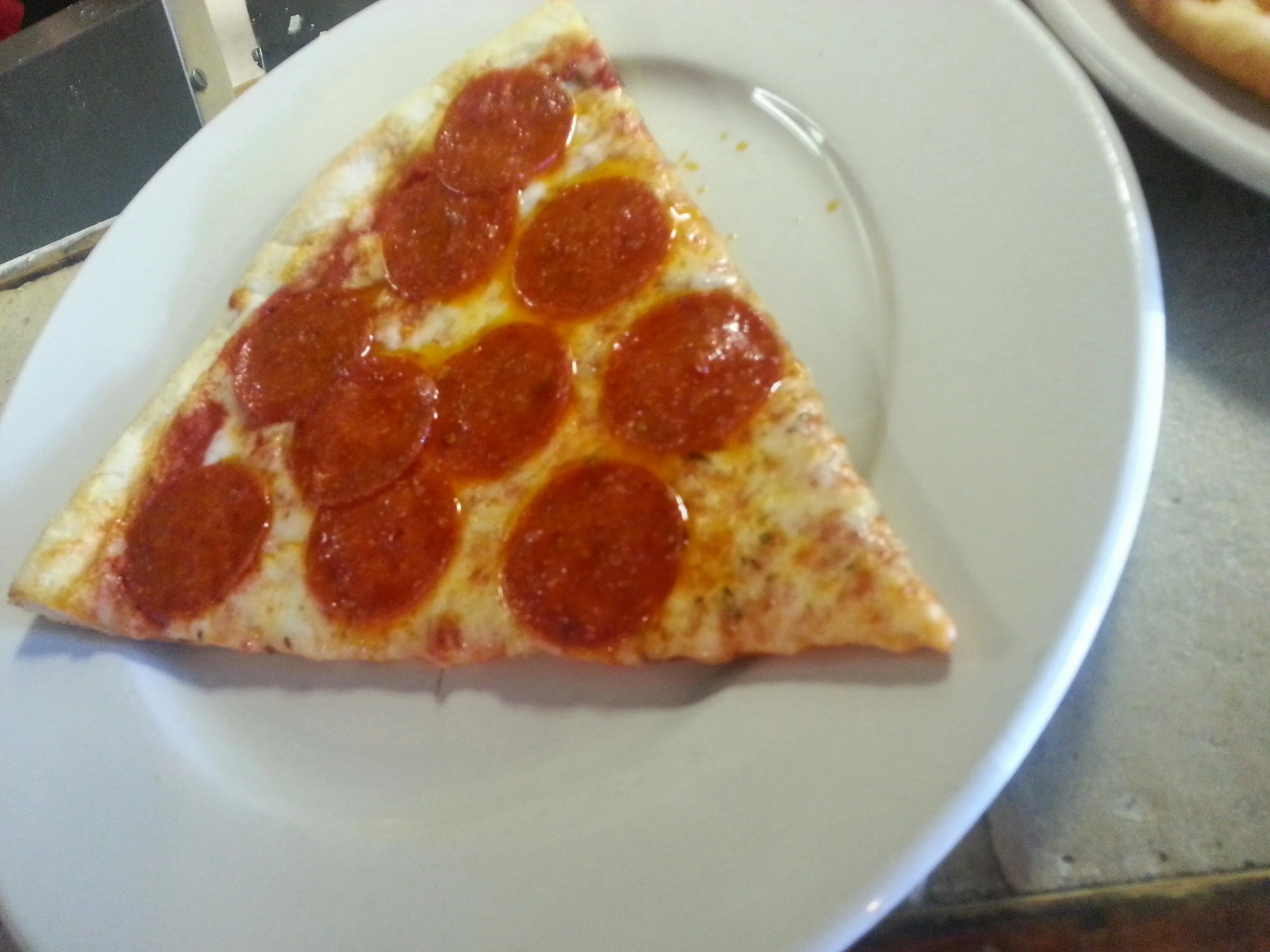 Slice of classic pepperoni pizza on a white plate