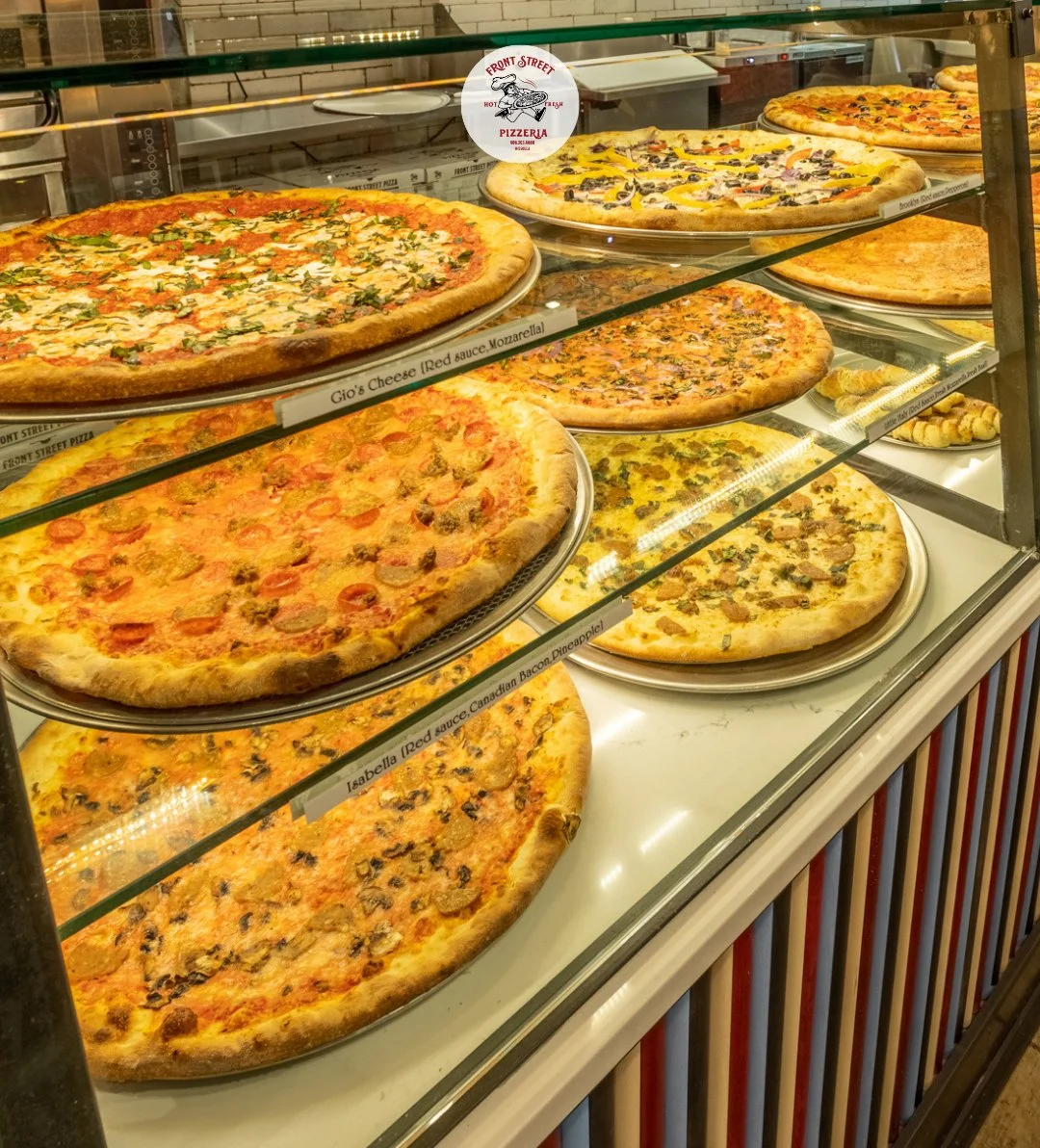 A display of various pizzas in a glass case, showcasing different toppings and styles.