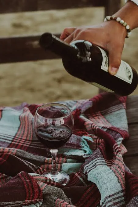 Pouring red wine into a glass on a plaid blanket