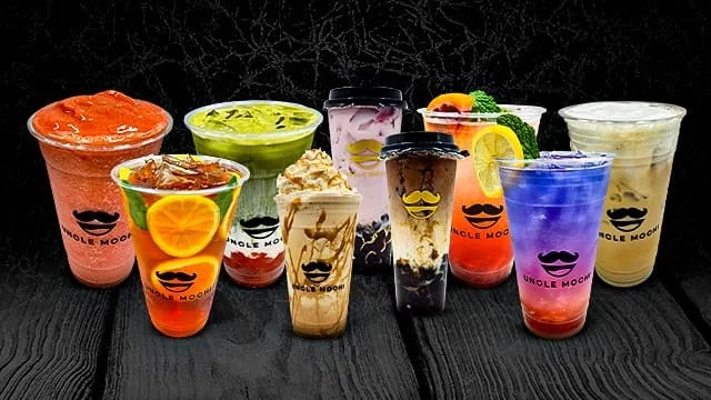 A colorful assortment of beverages in clear cups, featuring various flavors and garnishes. Each drink is topped with distinct decorations, showcasing a vibrant presentation.